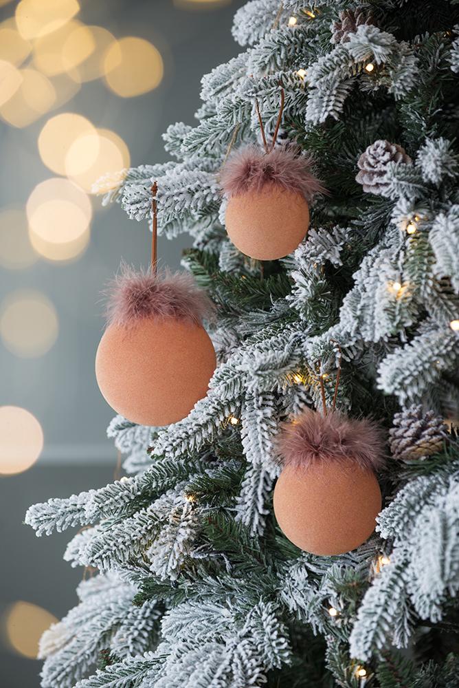 Closeup of a flocked Christmas tree branch with four plush orange round ornaments trimmed with faux fur