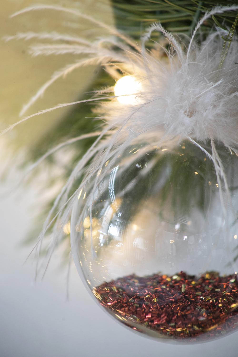 Clear glass Christmas bauble filled with rose gold glitter and white feathers