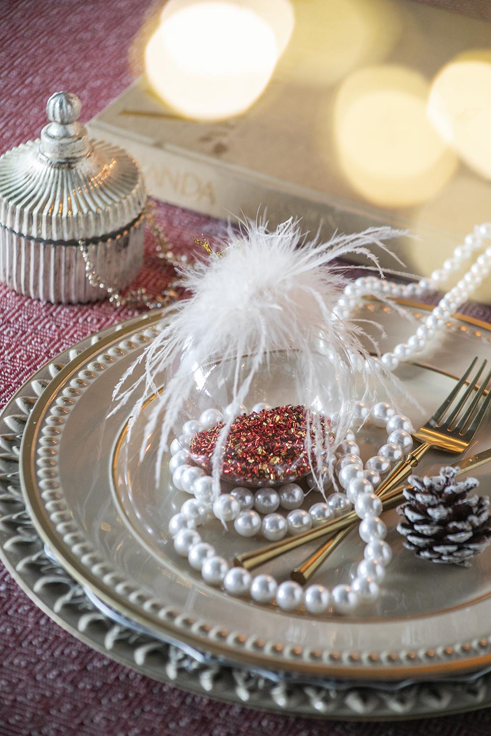 Elegant gold cutlery set with faux pearl strands and a decorative pine cone on a table setting