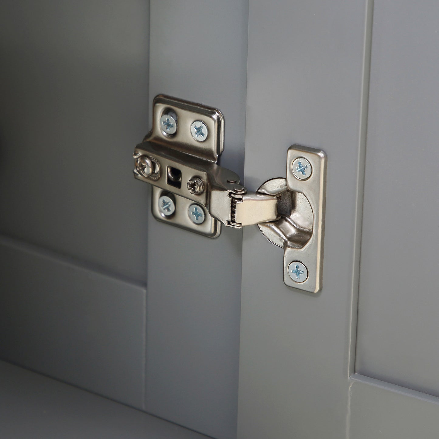 Closeup of a brushed nickel cabinet hinge on a grey wooden door panel showing screw details
