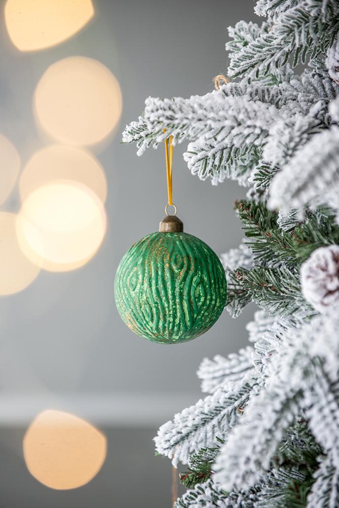 Textured green Christmas ornament with gold wood grain design hanging on a frosted tree branch