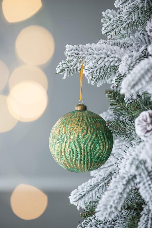 Green and gold textured bauble hanging on a frosted Christmas tree branch