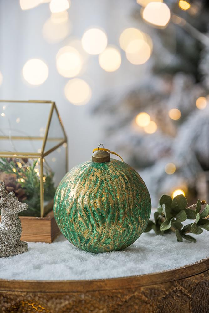Textured green and gold Christmas ornament with gold cap on a snowy surface