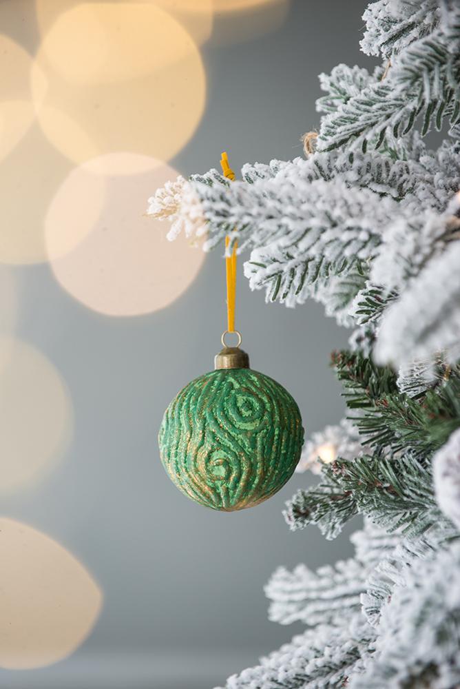 Textured green and gold Christmas ornament with swirling pattern hanging on a flocked tree branch
