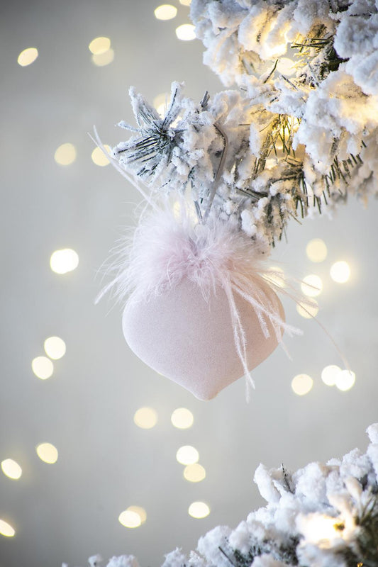 Soft pink fabric heart Christmas ornament with fluffy details hangs on a frosted branch with fairy lights