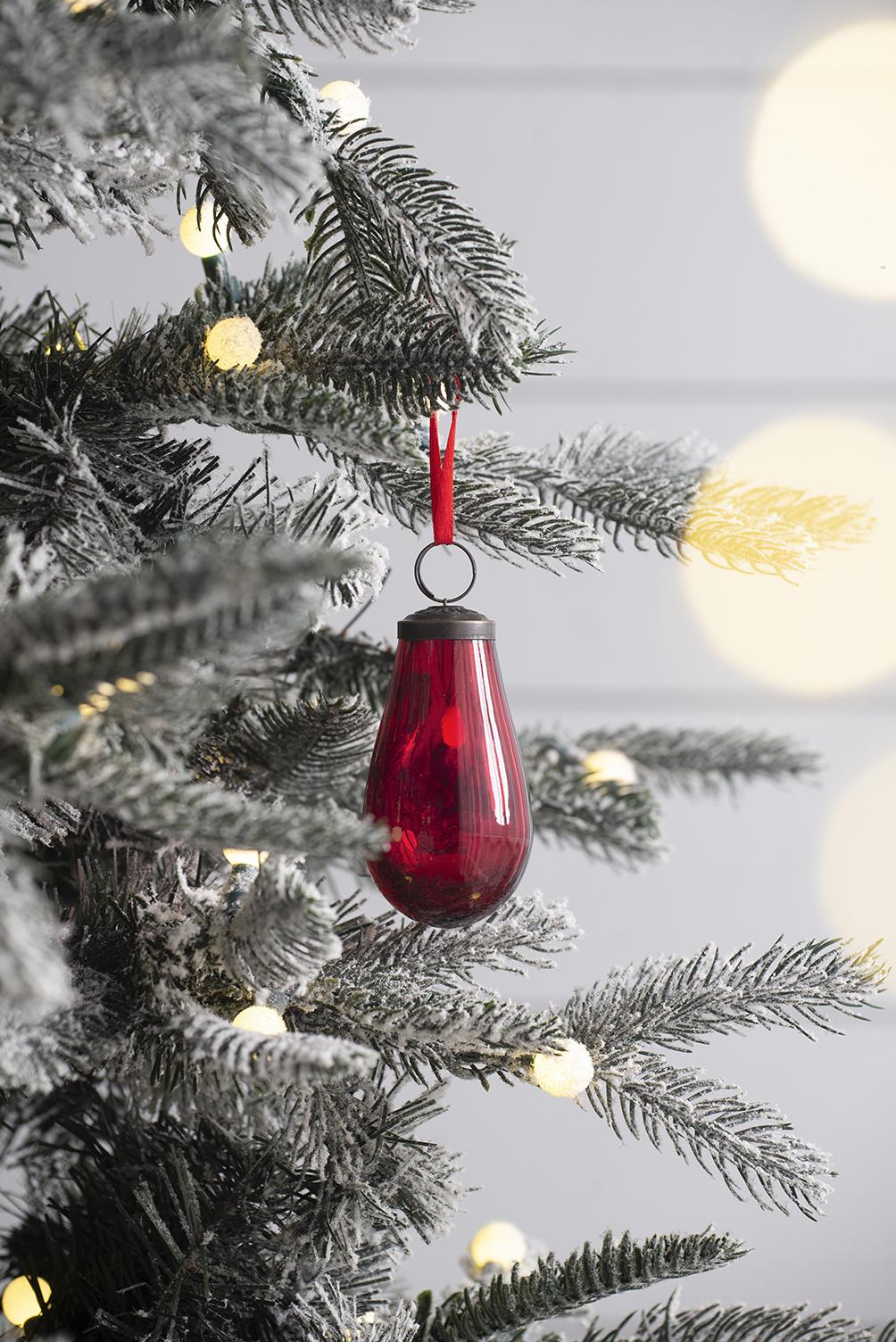 Red teardrop glass Christmas ornament with metal cap hanging on flocked tree branch