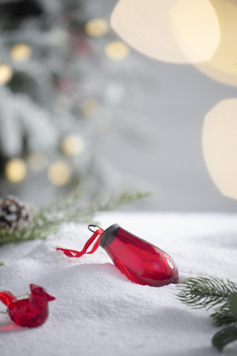 Red glass teardrop Christmas ornament with ribbon on snow