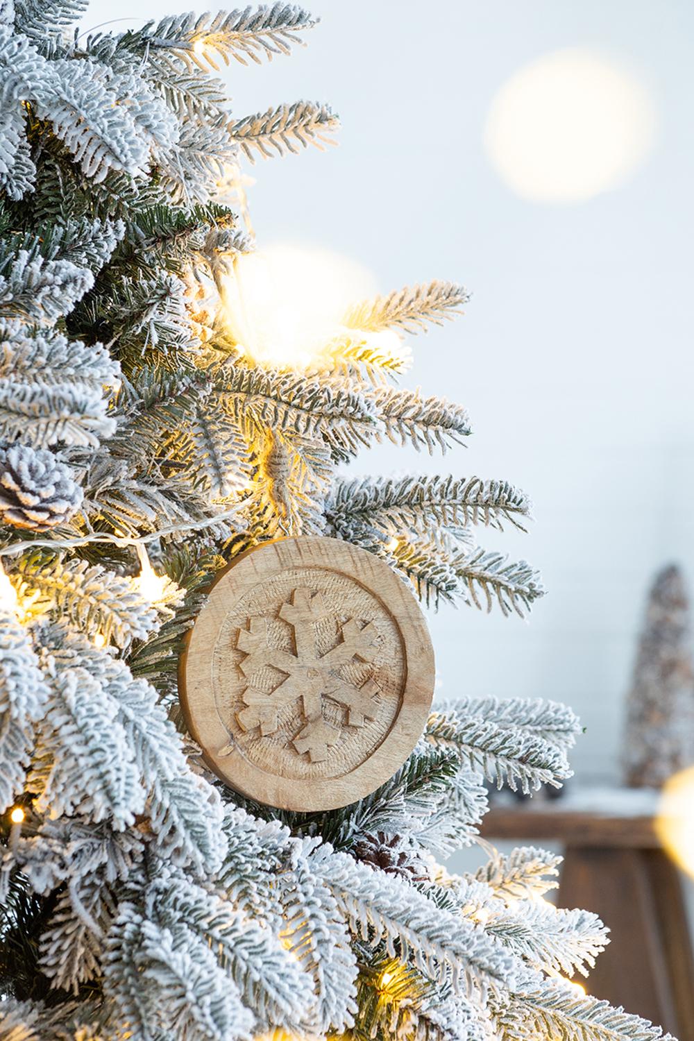 Wooden snowflake ornament hanging on a frosted Christmas tree with fairy lights