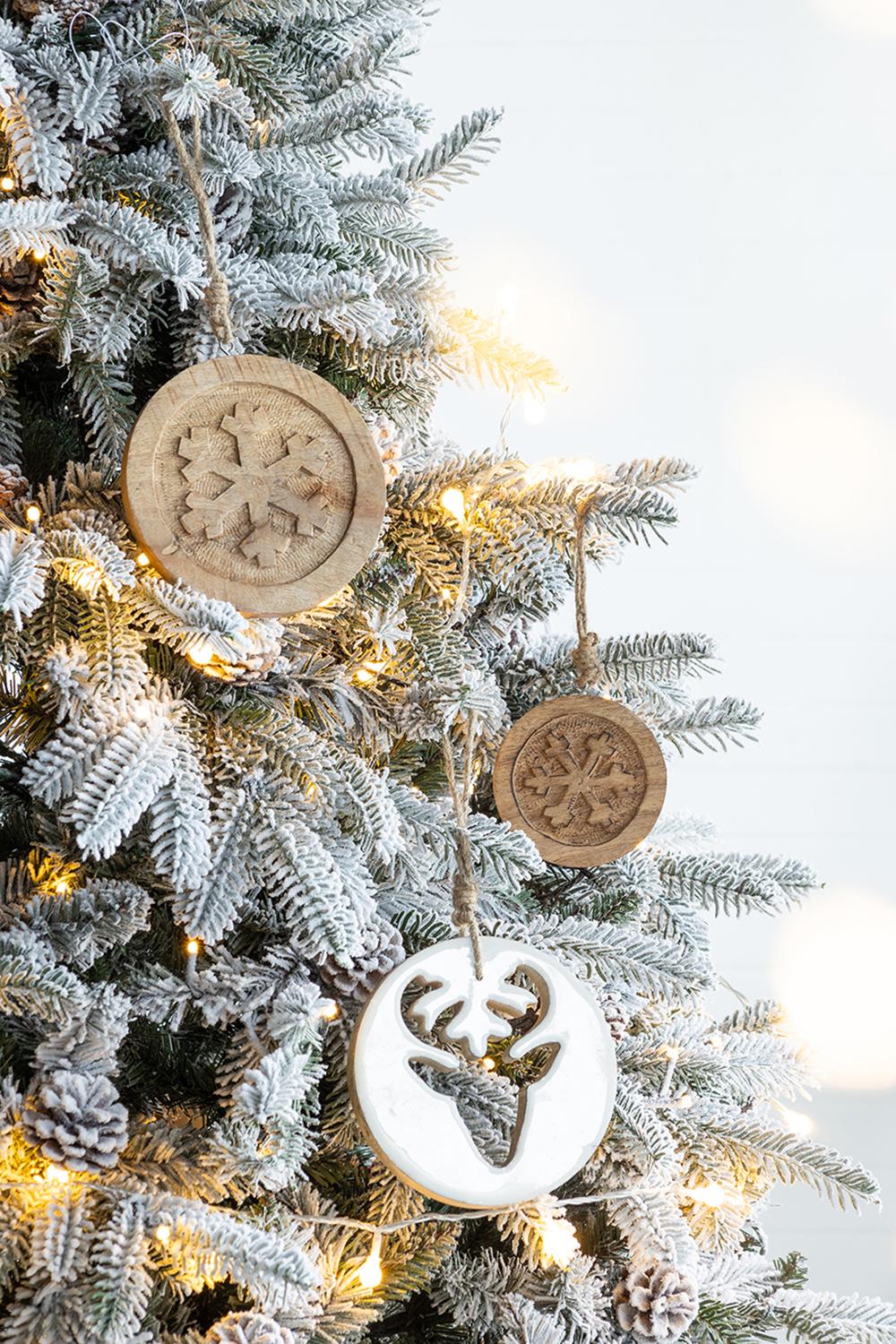 Round wooden snowflake ornament hanging on a frosted Christmas tree branch
