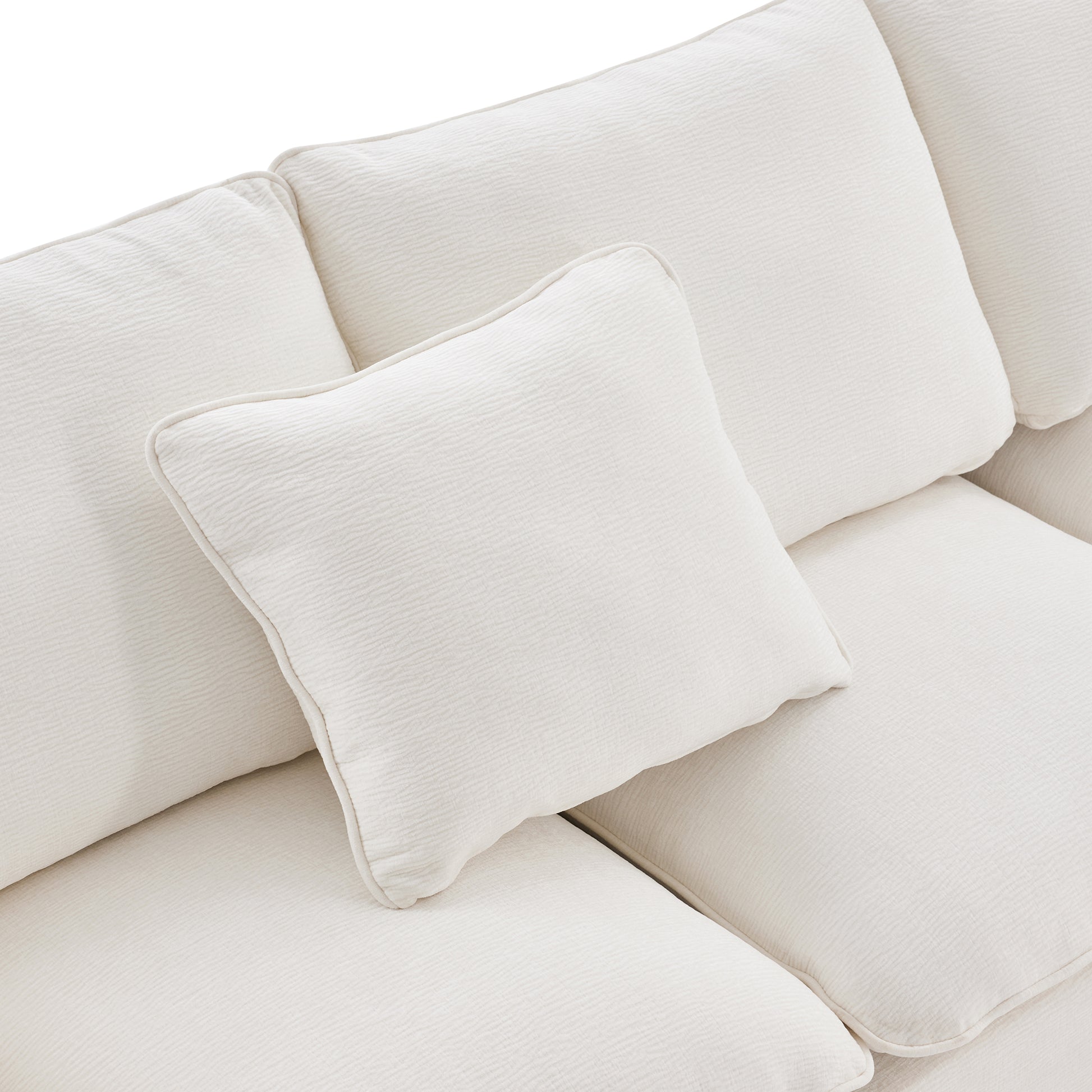 Close up of a textured cream couch with plush cushions and a decorative throw pillow