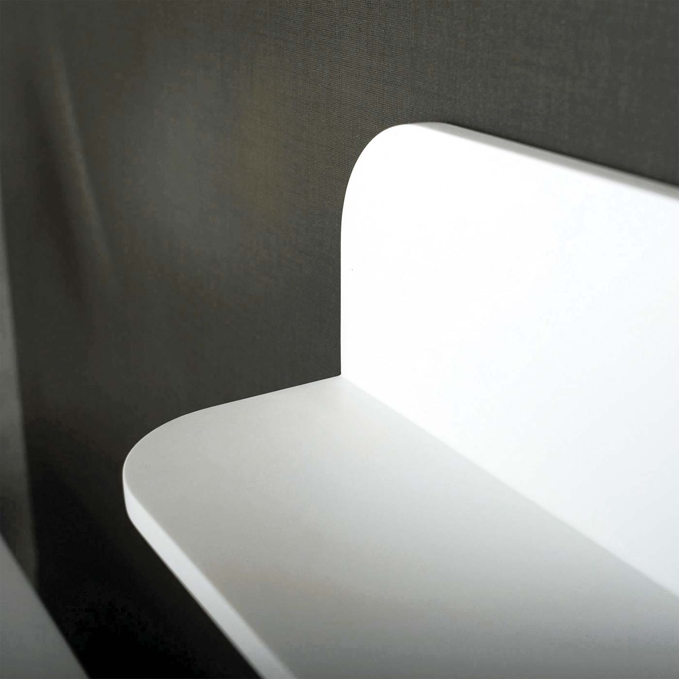 Closeup of a matte white floating shelf with rounded edges against a dark textured wall