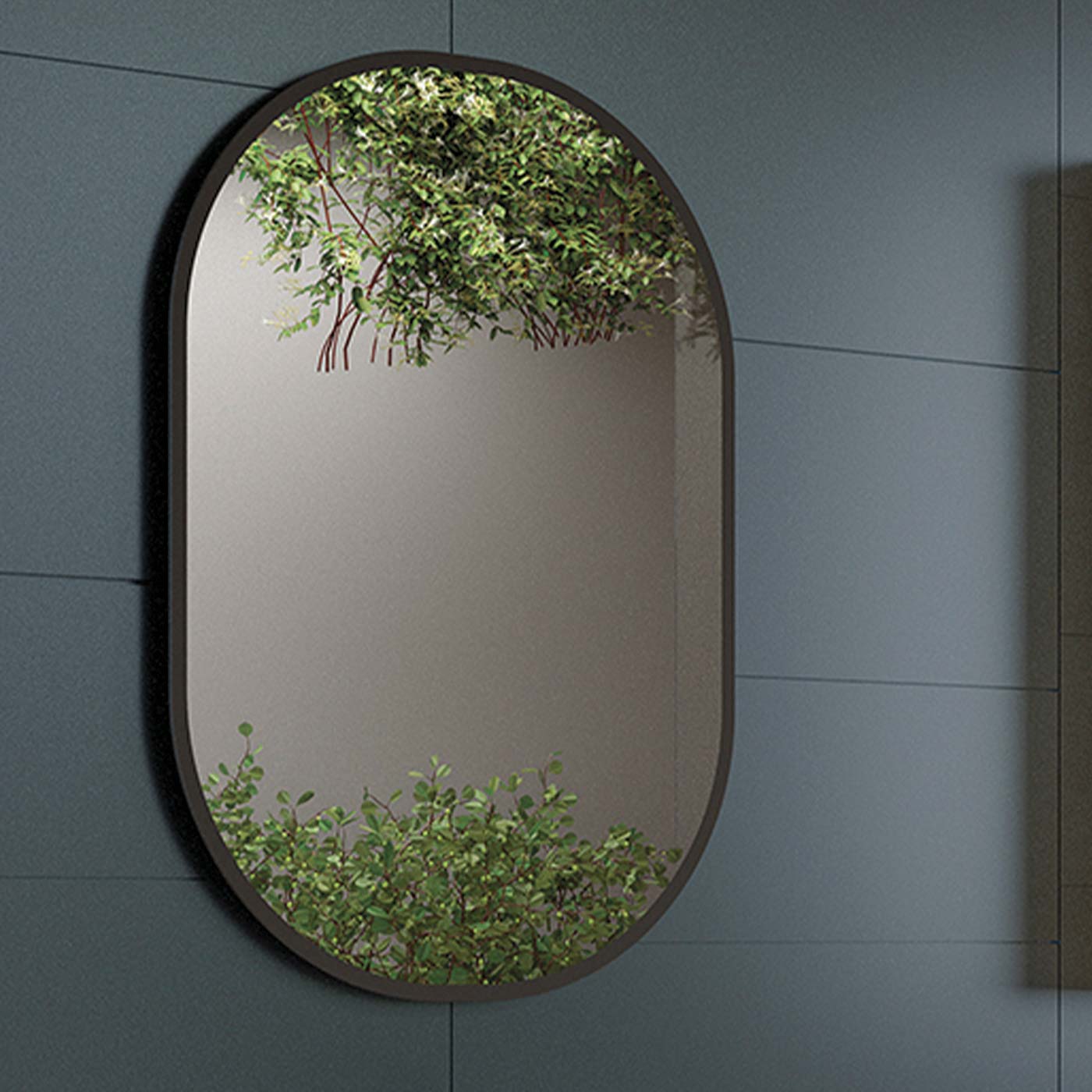 Oval black framed bathroom mirror reflecting green foliage and a modern wall