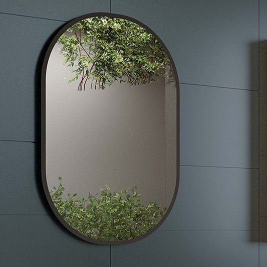 Oval black framed bathroom mirror reflecting green foliage and a modern wall
