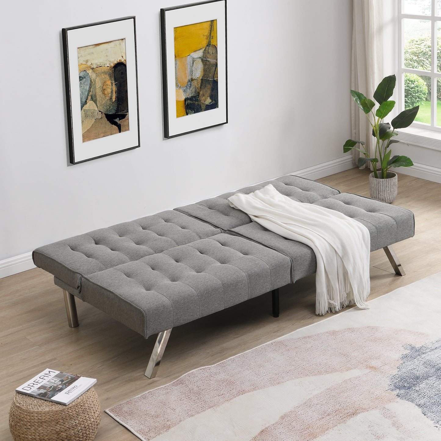 Tufted gray fabric futon sofa with silver metal legs and white throw blanket