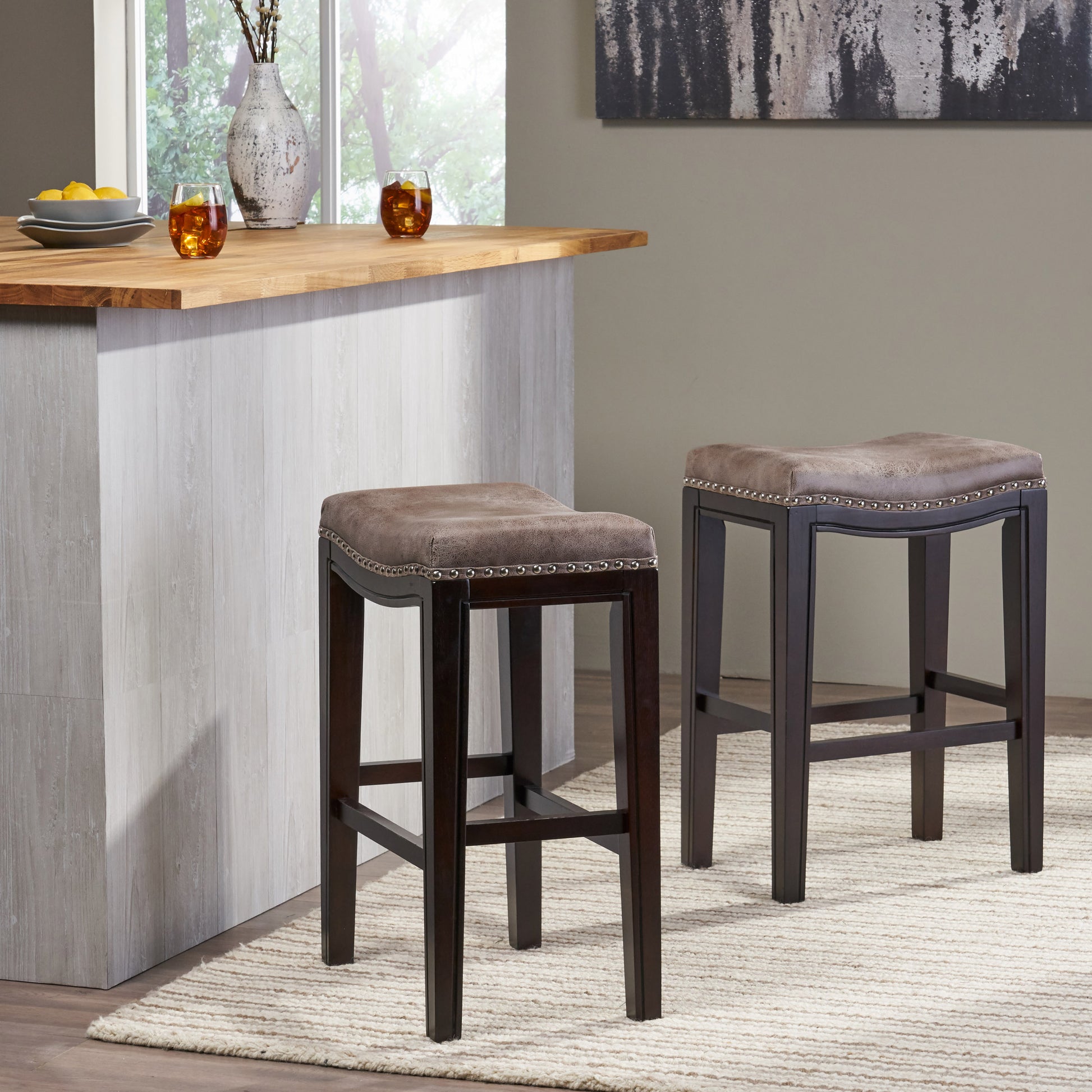 Two brown faux leather saddle bar stools with nailhead trim and dark wood legs