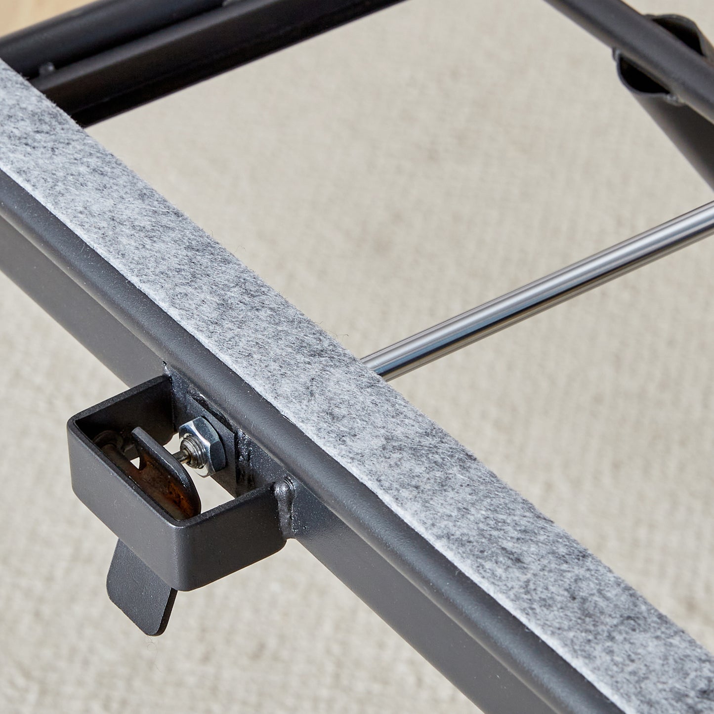 Black metal bed frame detail with gray felt padding and securing bolt for mattress support