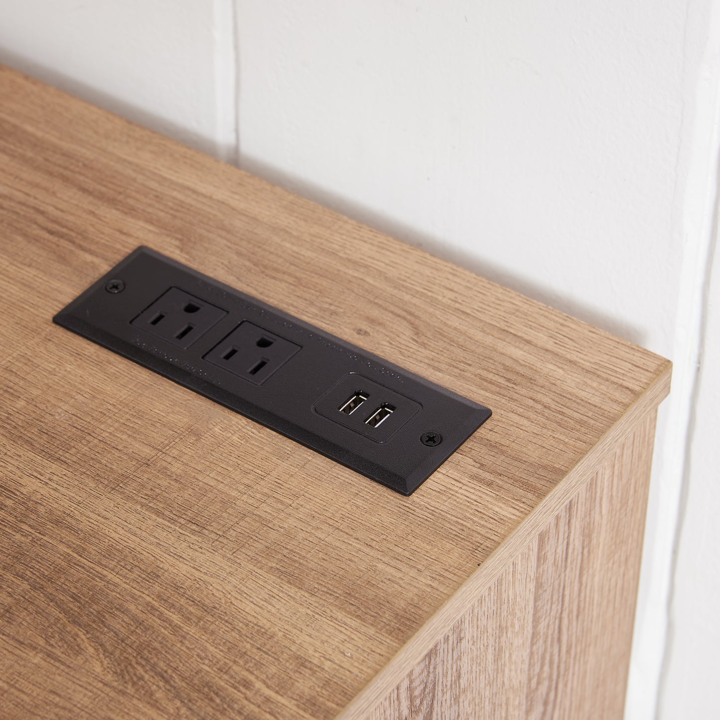 Recessed black power outlet with two USB ports on a wood grain surface