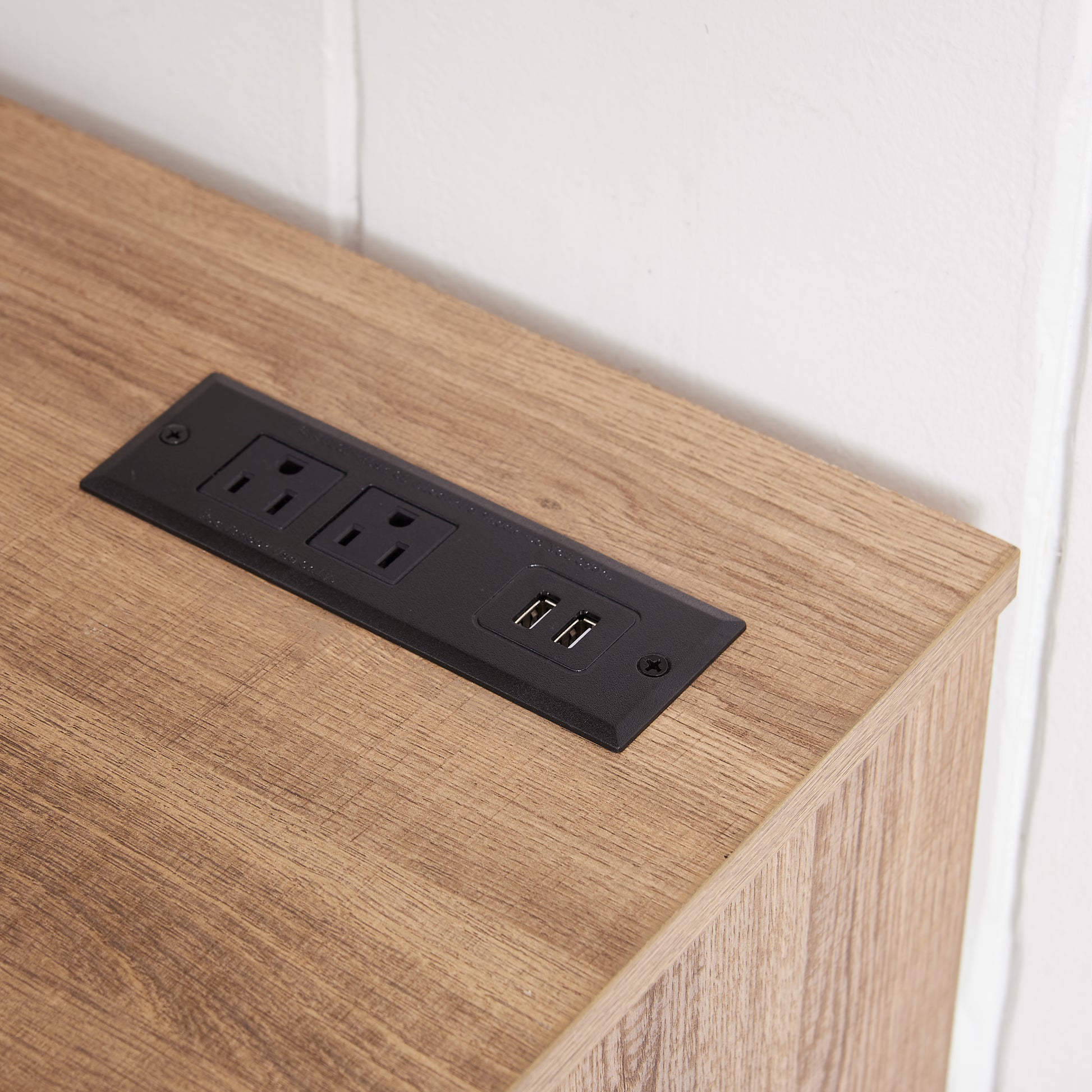 Recessed black power outlet with two USB ports on a wood grain surface
