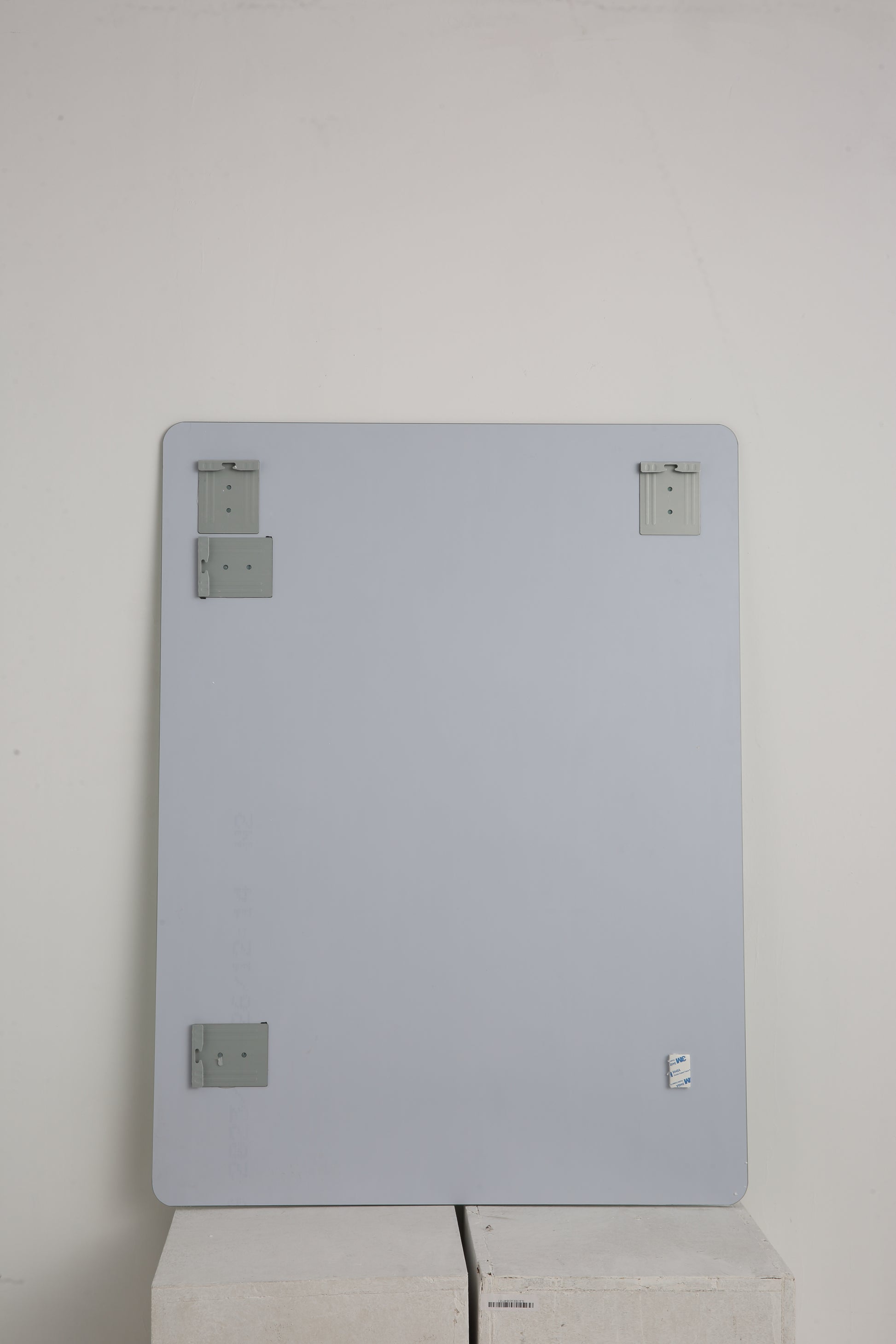 Back view of a large rectangular frameless bathroom mirror with gray mounting brackets attached