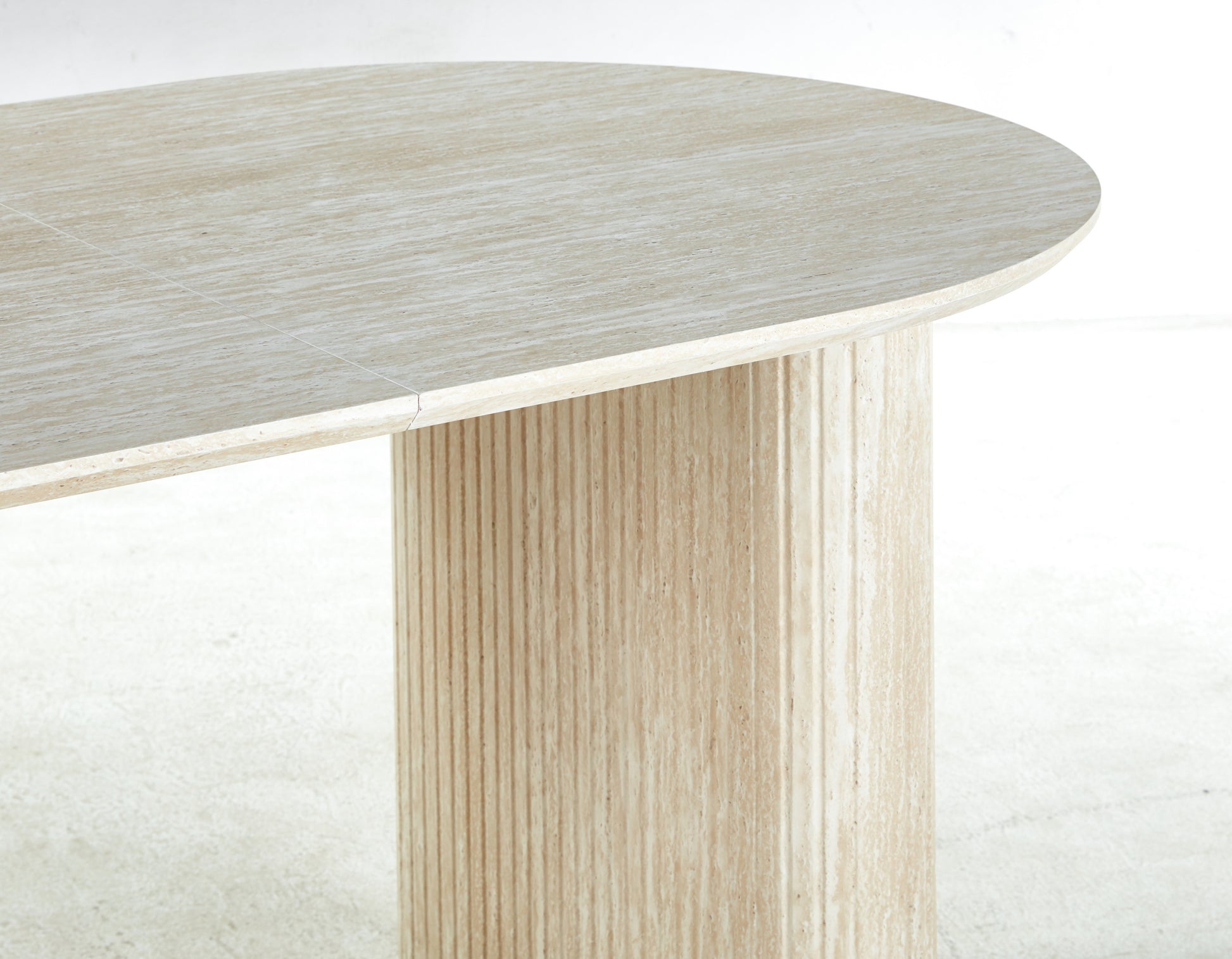 Beige travertine dining table with a smooth oval top and fluted pedestal base