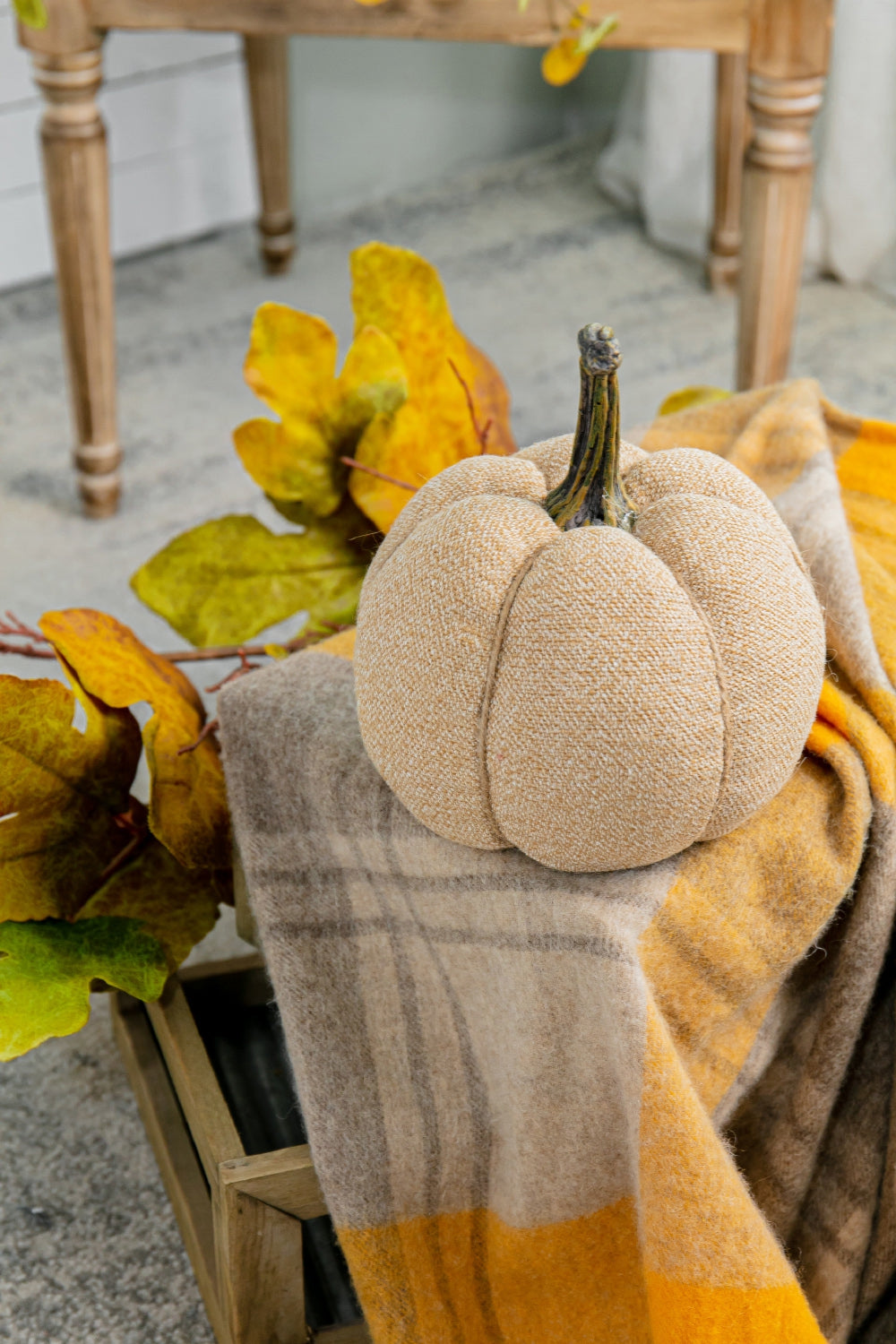 Textured beige fabric pumpkin with brown stem on a plaid throw