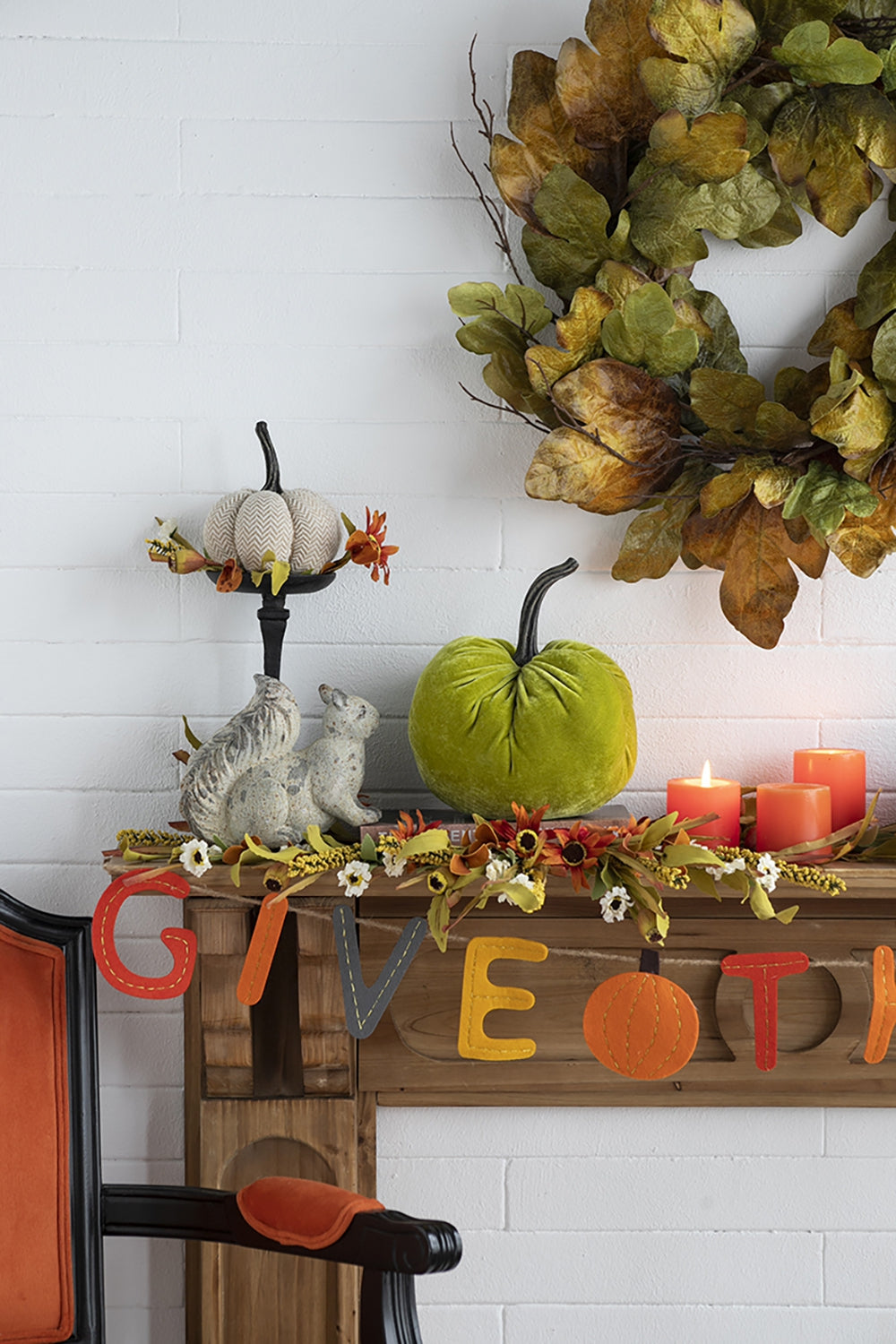 A festive autumn mantel display featuring a plush green pumpkin and two ceramic squirrels