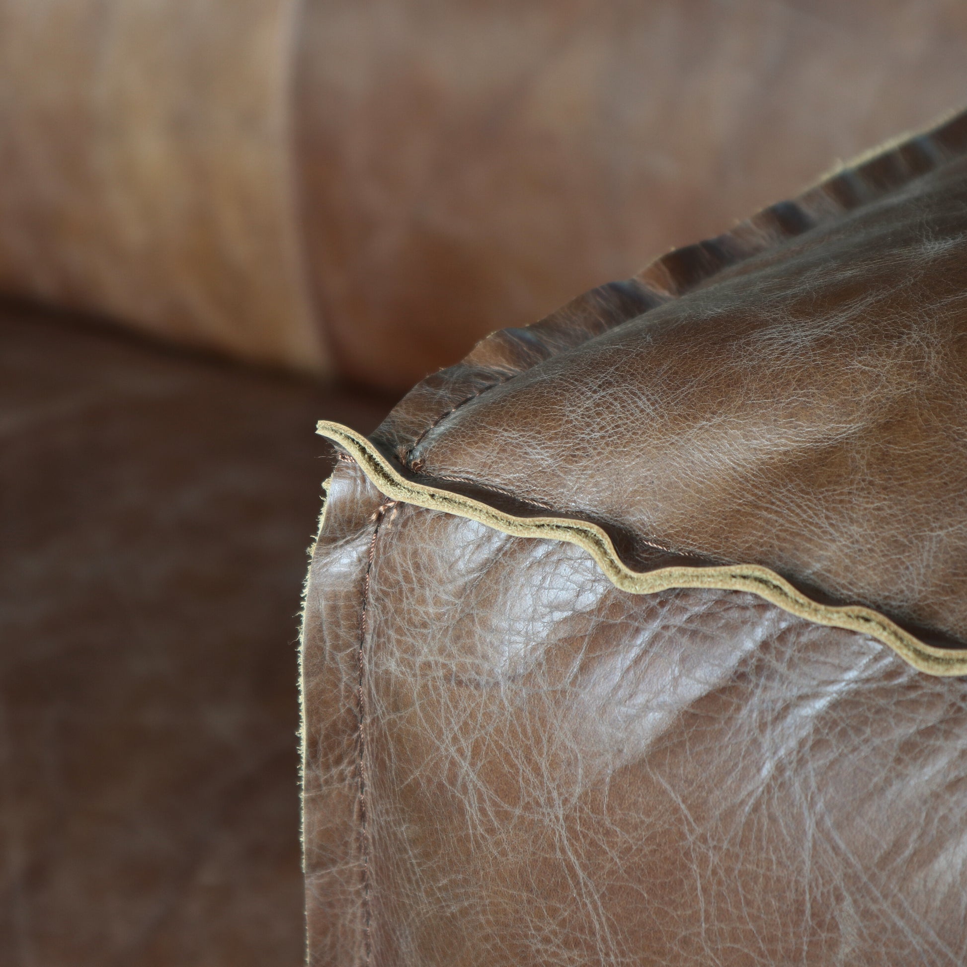 Closeup of distressed brown leather couch corner with visible stitching detail