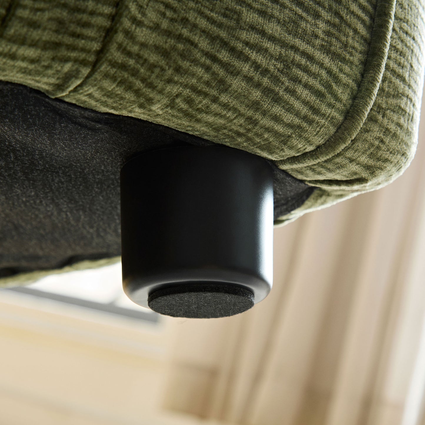 Closeup of textured olive green fabric on a sofa with a black cylindrical leg