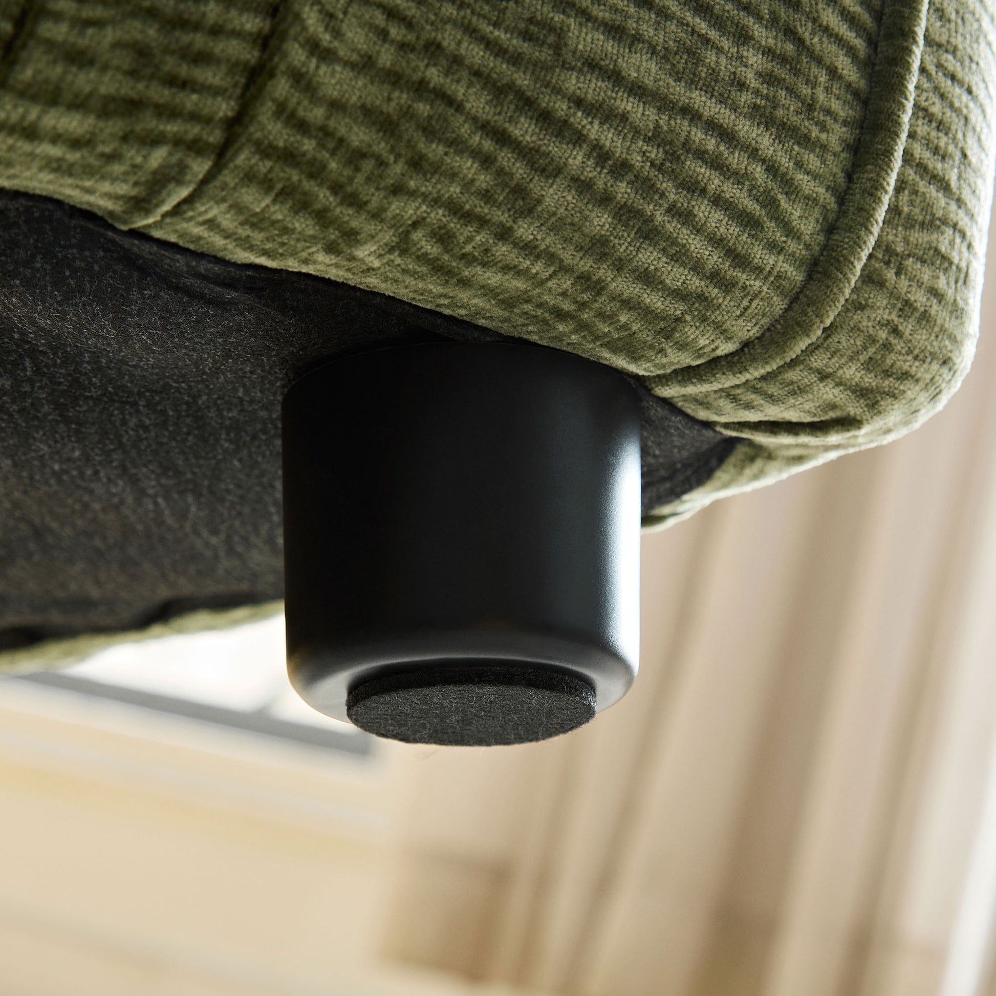 Closeup of textured olive green fabric on a sofa with a black cylindrical leg