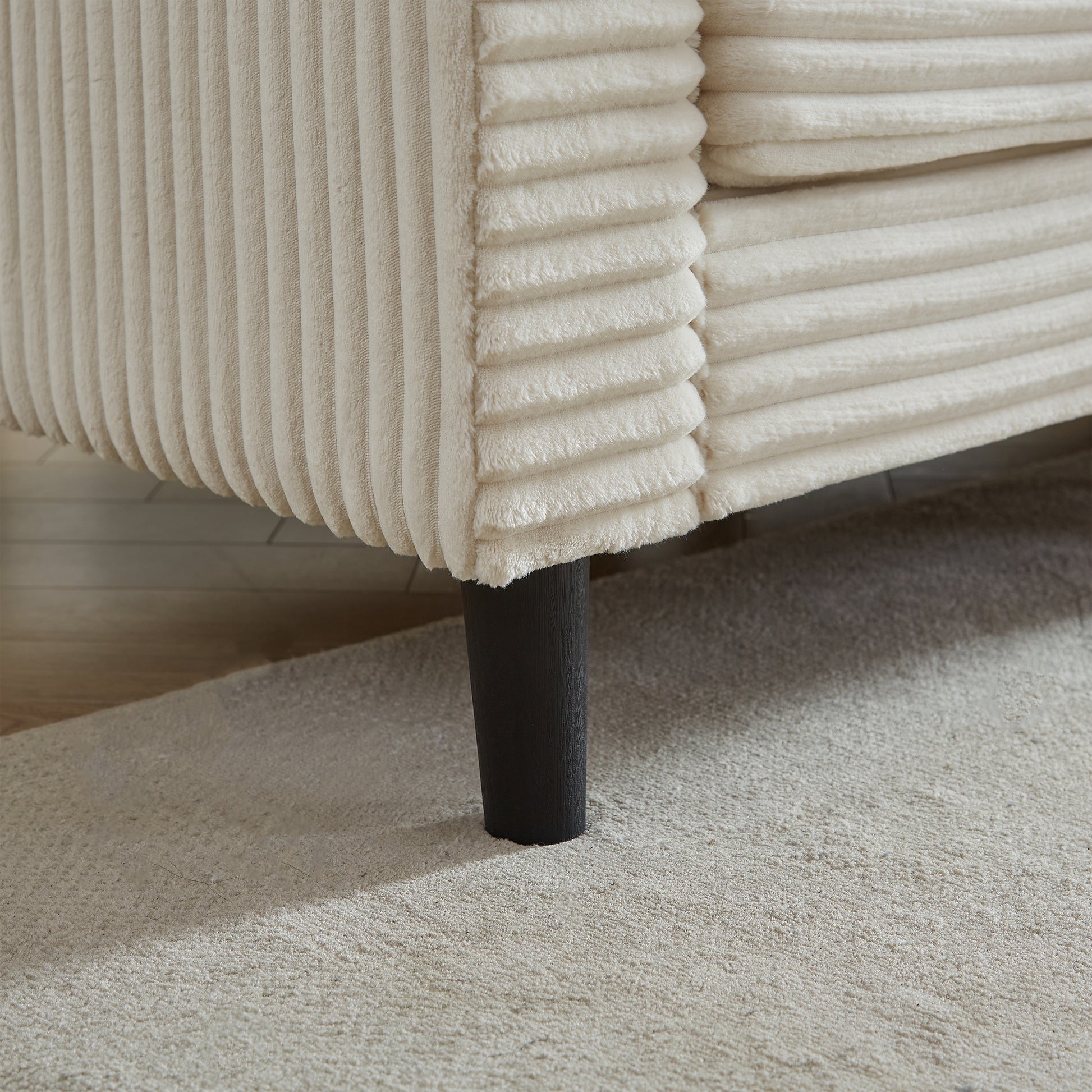 Cream corduroy armchair detail with textured fabric and dark wooden leg on a rug