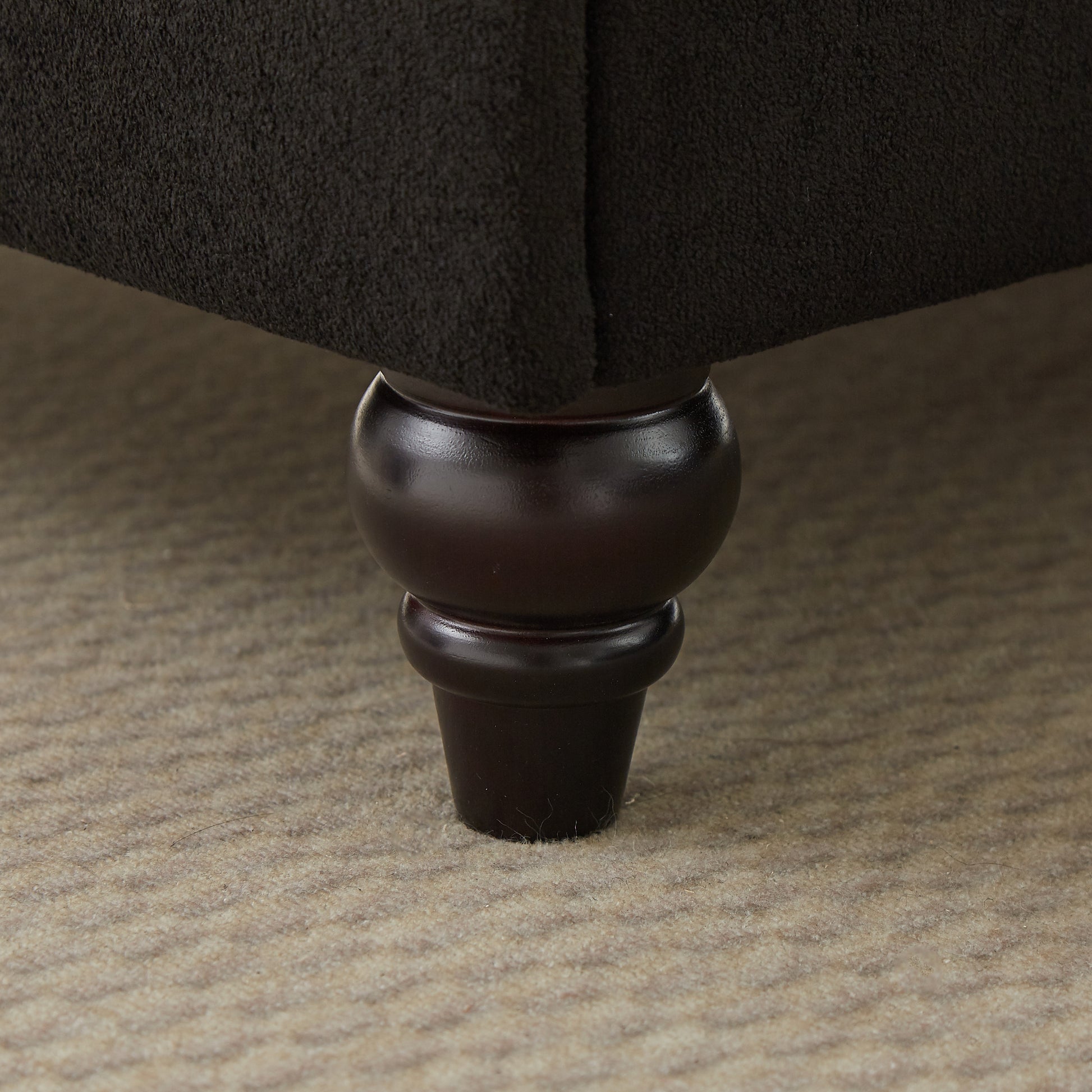 Dark brown upholstered sofa leg with ornate turned wood detailing on carpet