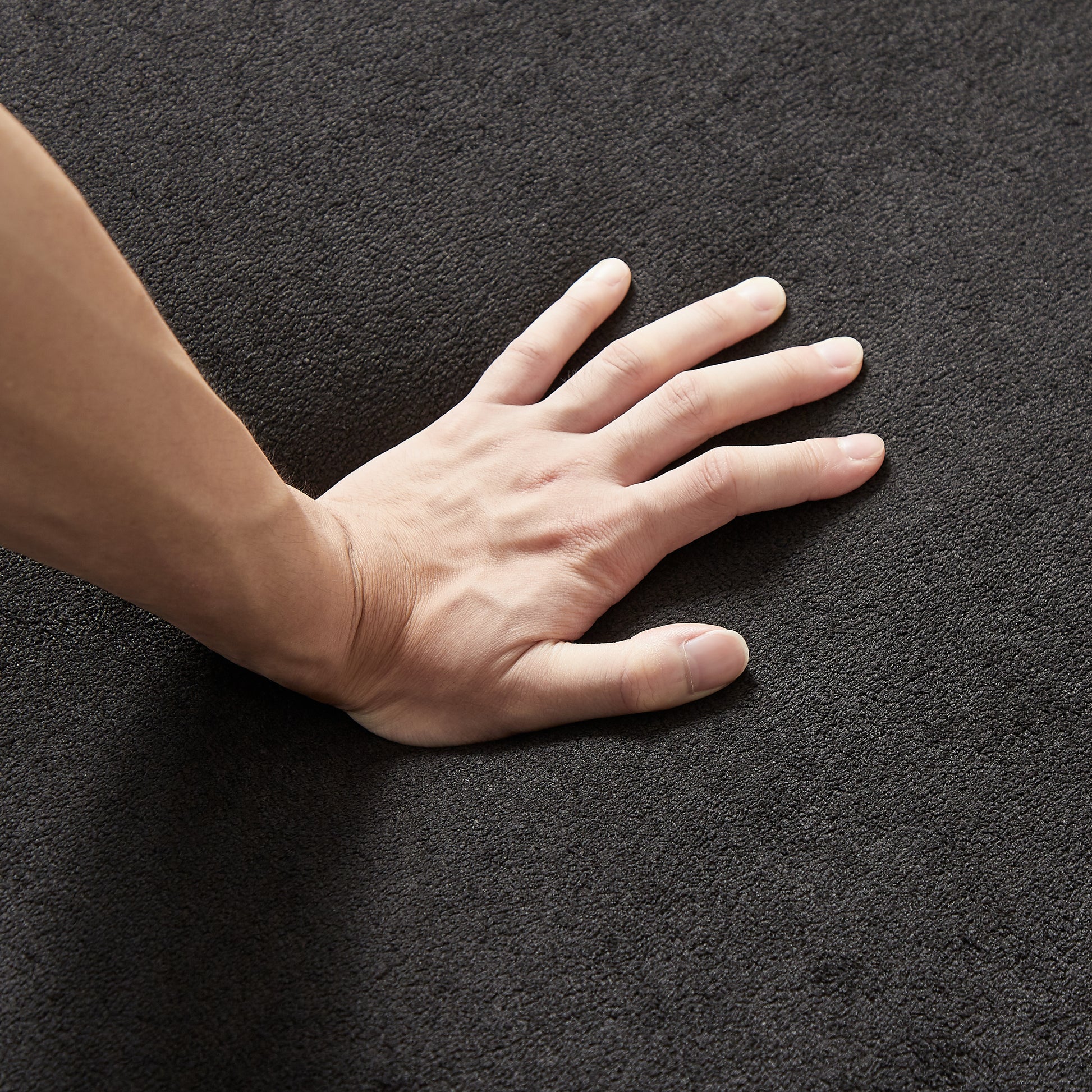 Hand pressing into plush charcoal grey carpet texture sample for comfort