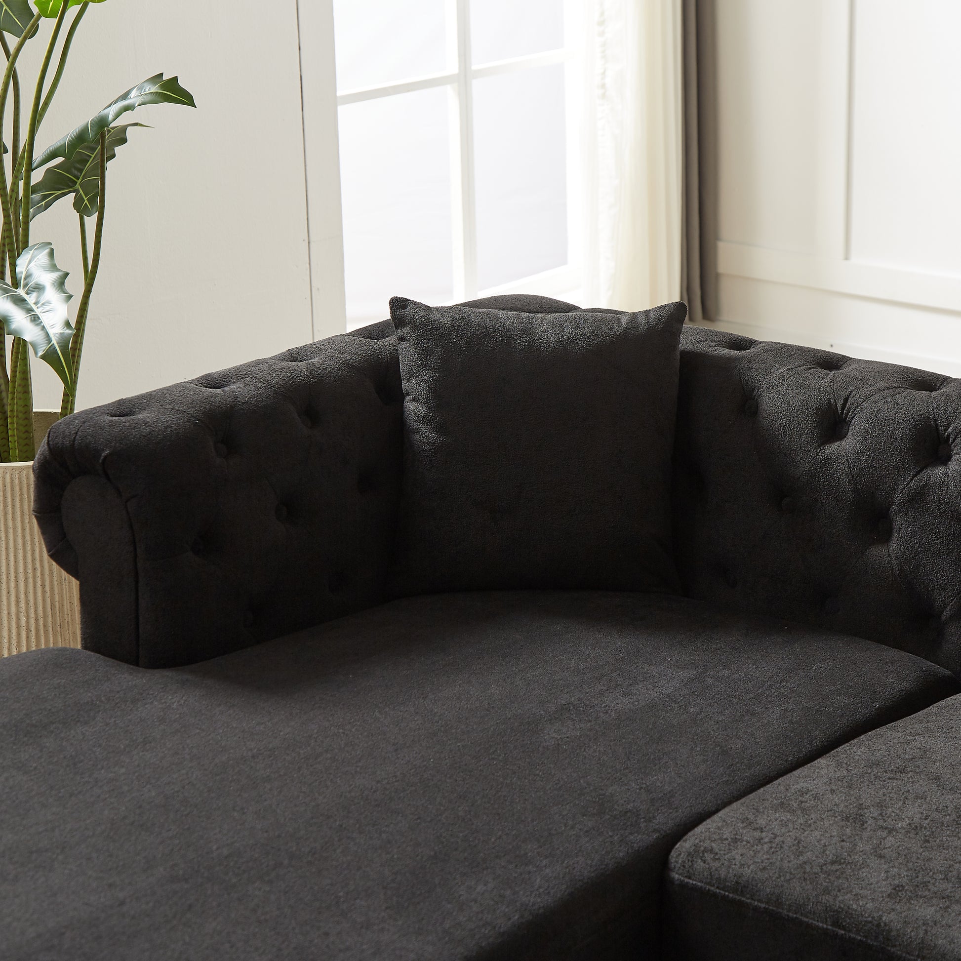 Dark grey tufted fabric sectional sofa with a plush accent pillow
