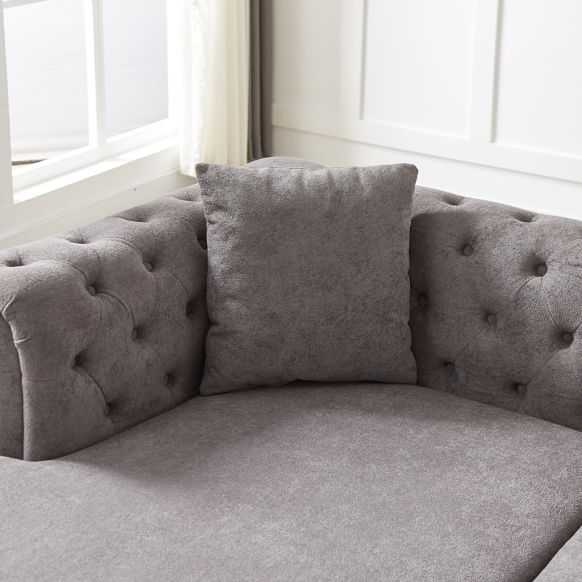 Closeup of a gray chenille tufted sofa with a matching throw pillow