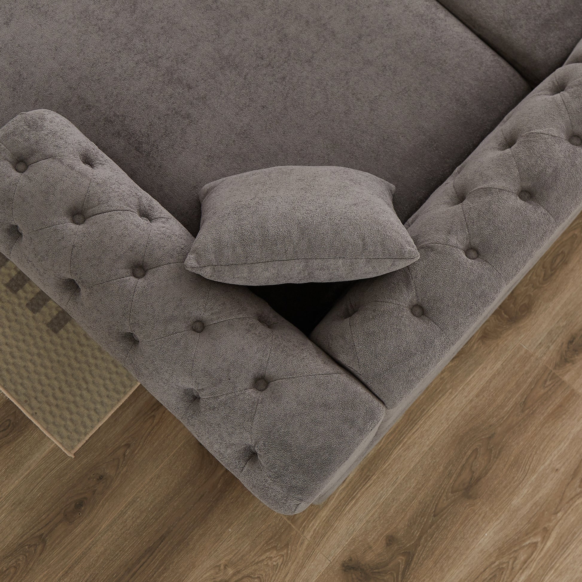 Tufted grey fabric sofa corner with a small grey pillow and wooden floor