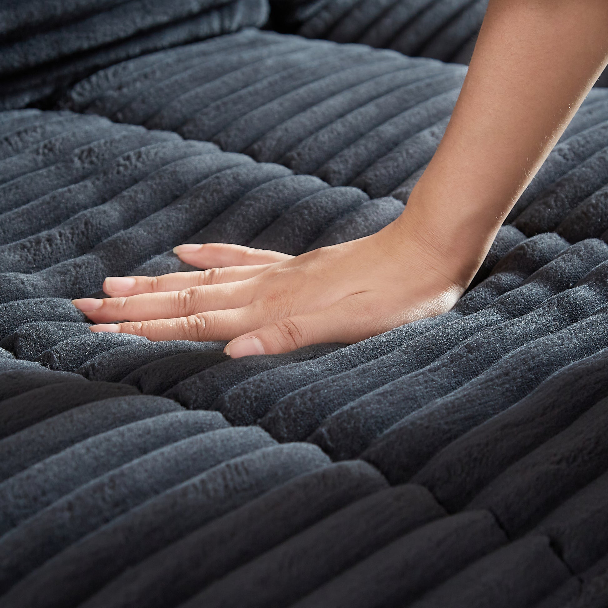 Closeup of a hand testing the soft texture of a charcoal grey corduroy sofa cushion