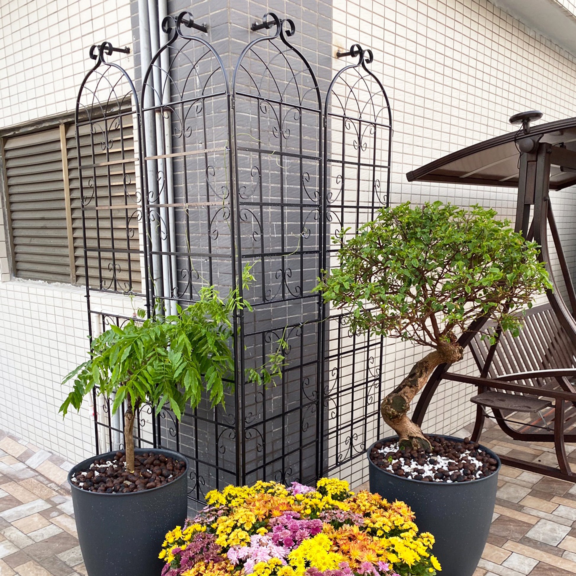 Tall black metal garden trellis with ornate scrollwork and arched top panel