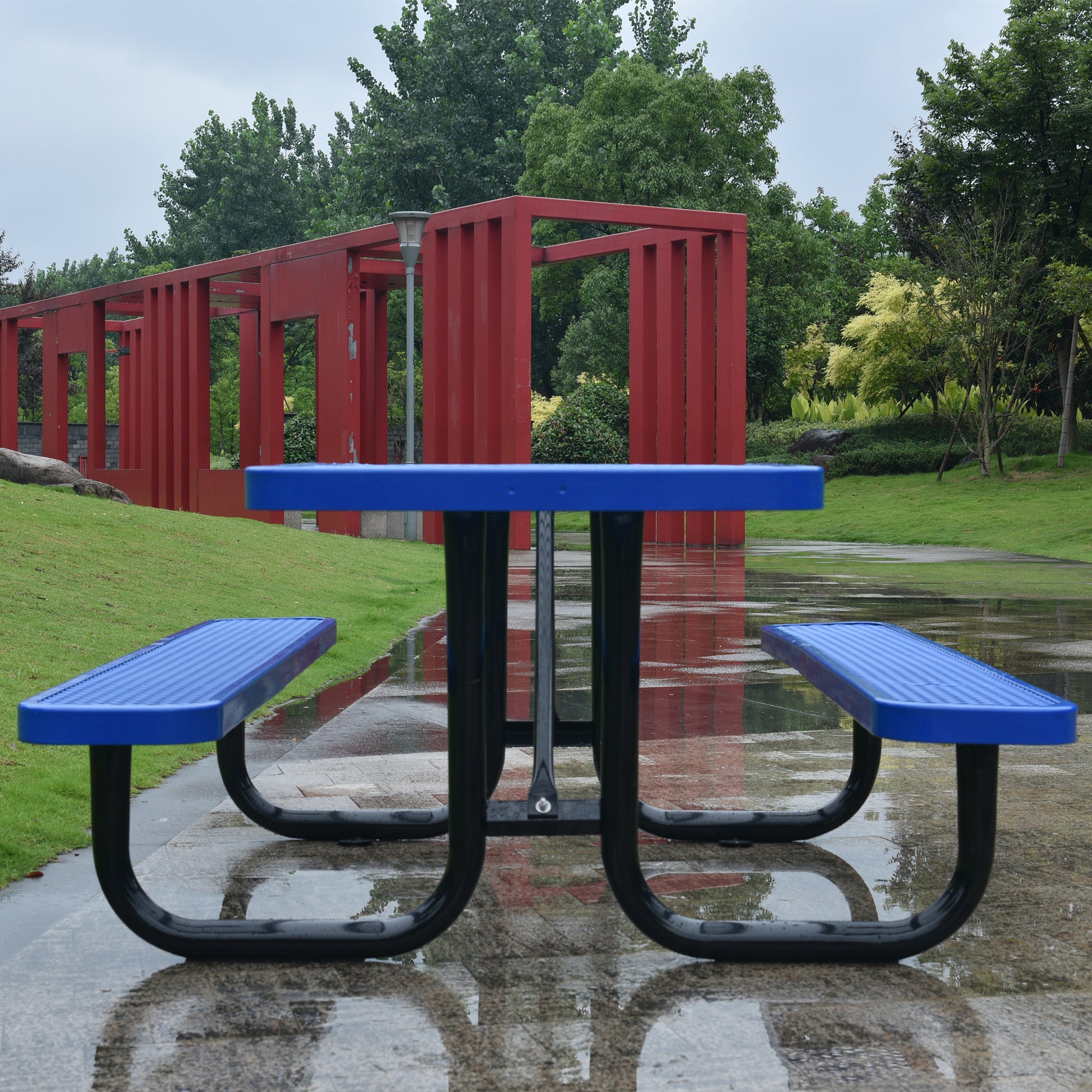 Blue perforated metal picnic table with black frame on wet paved ground outdoors