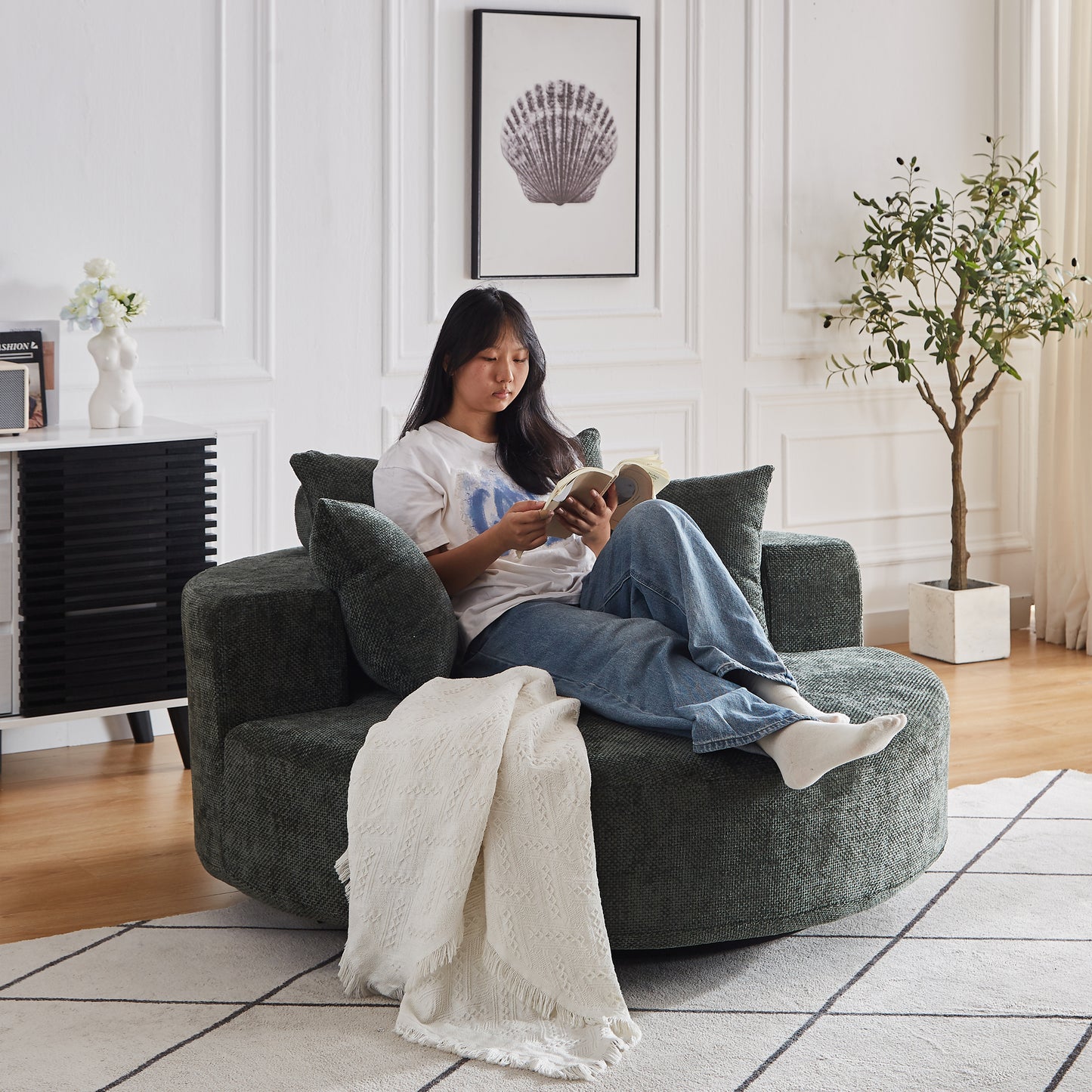 Deep green textured round couch with plush cushions and a white throw blanket