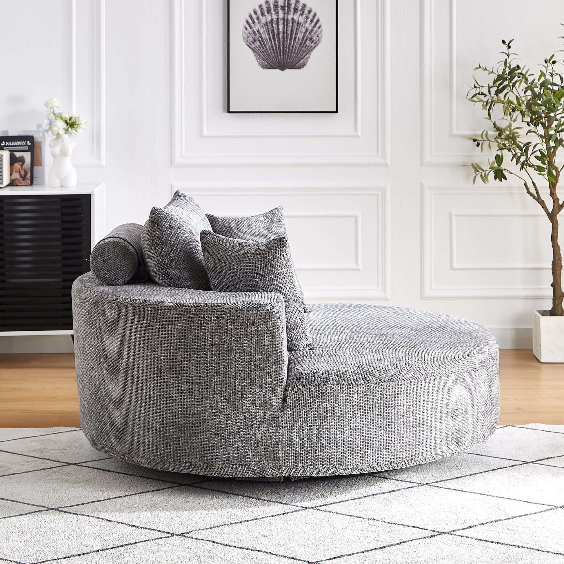 Round grey fabric chaise lounge with accent pillows on a rug