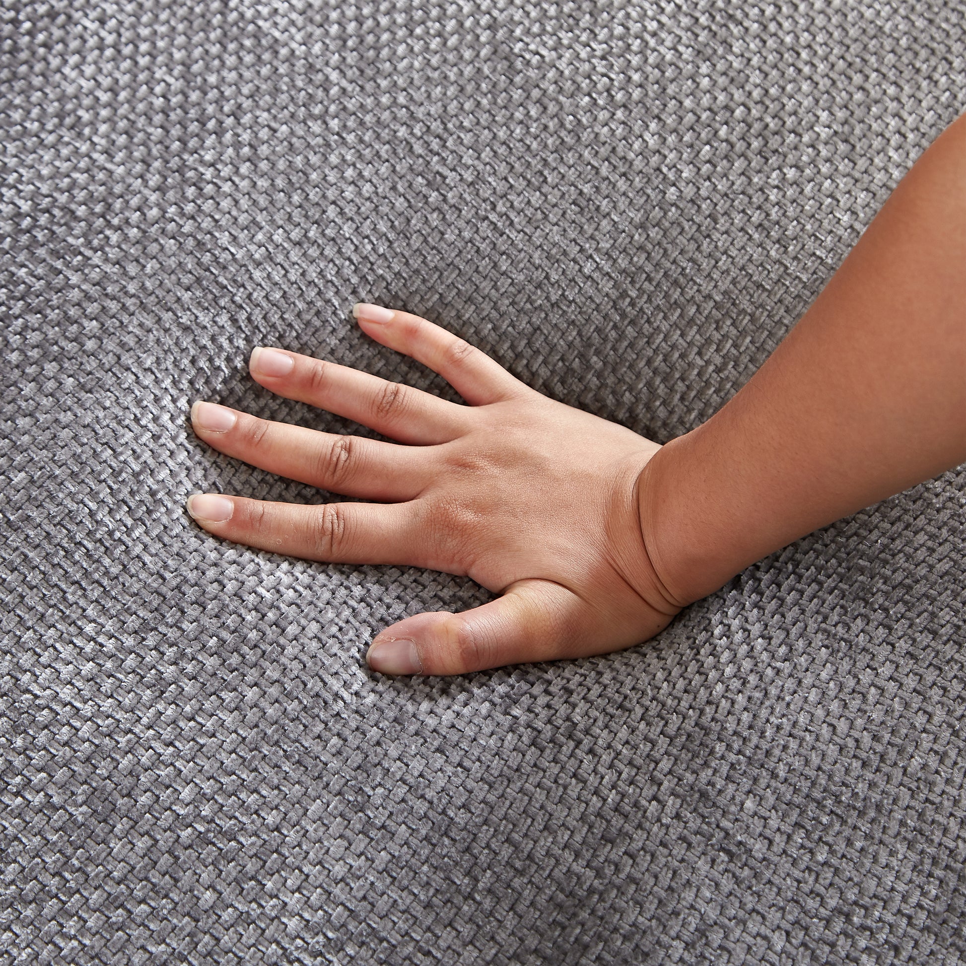 Closeup of hand pressing into textured grey fabric sofa upholstery showing softness and durability