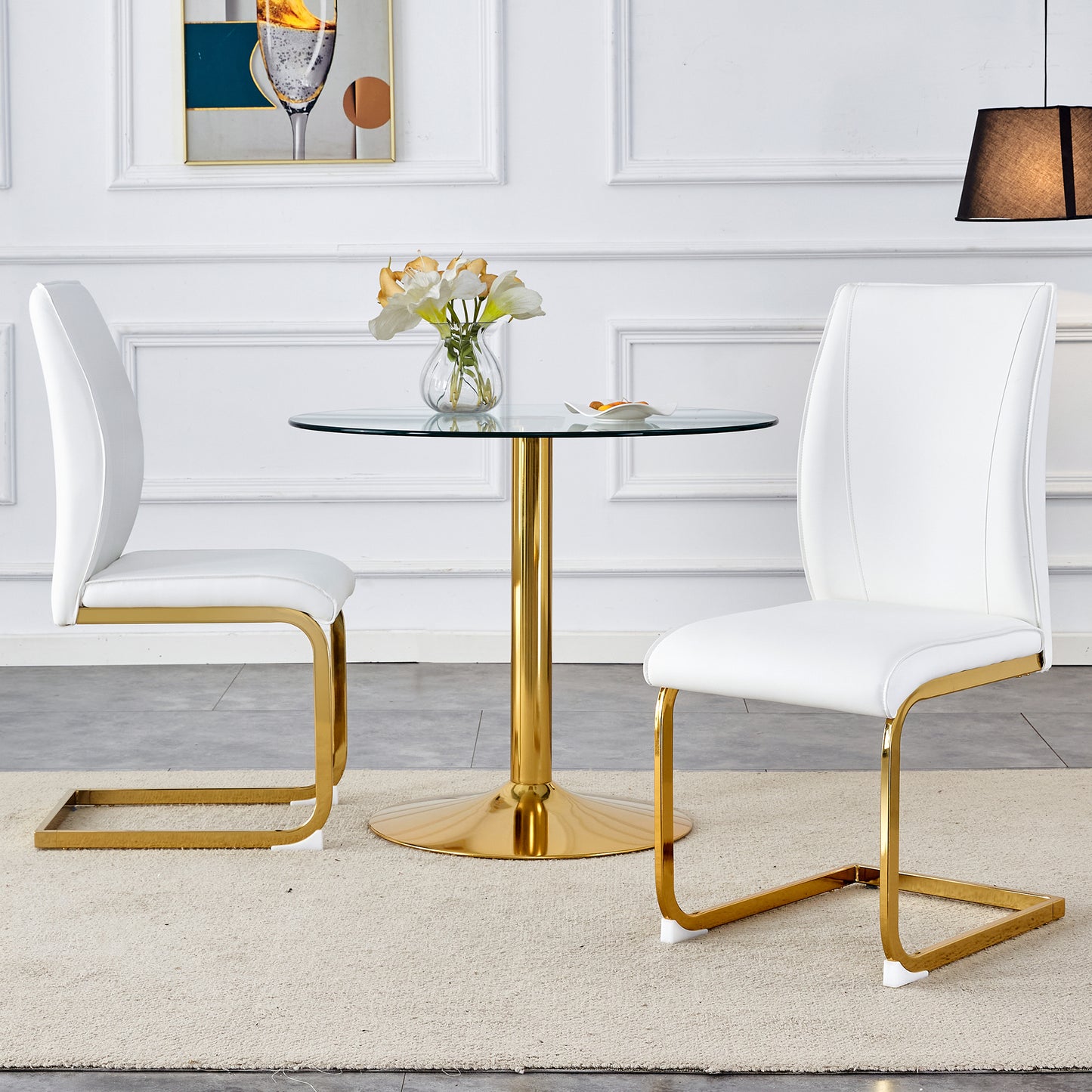 Two white faux leather dining chairs with gold metal legs arranged around a round glass table