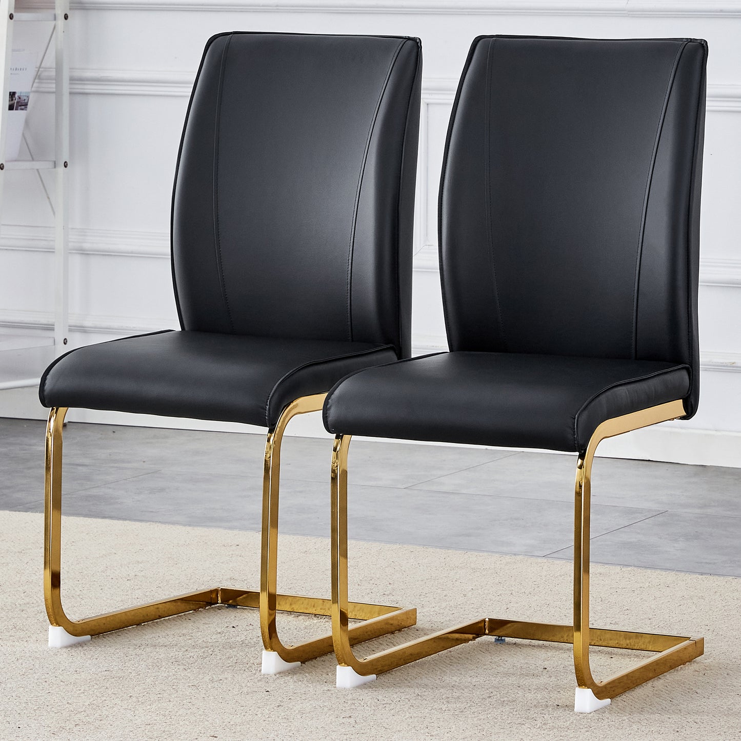Two sleek black faux leather dining chairs with polished gold sled legs