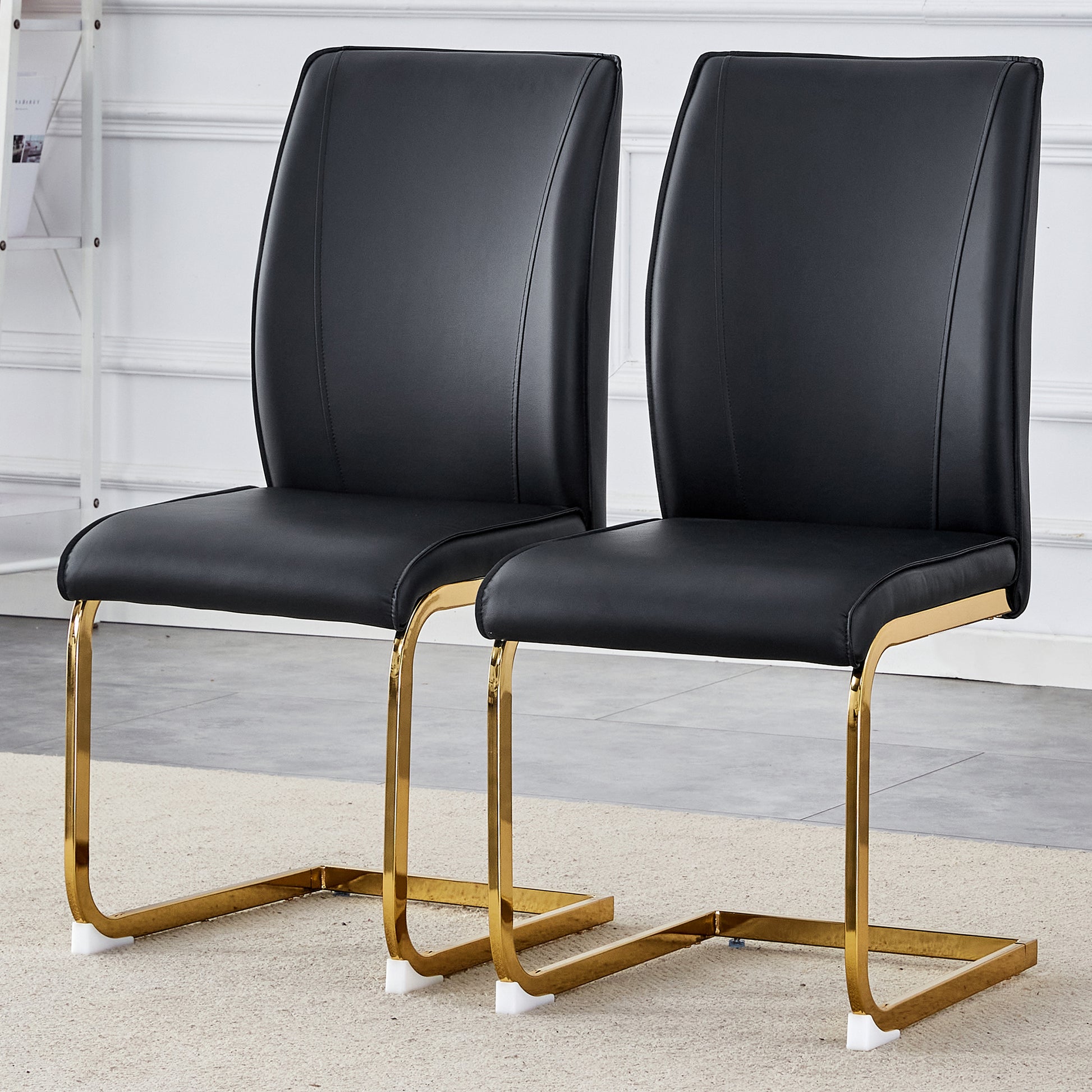 Two sleek black faux leather dining chairs with polished gold sled legs