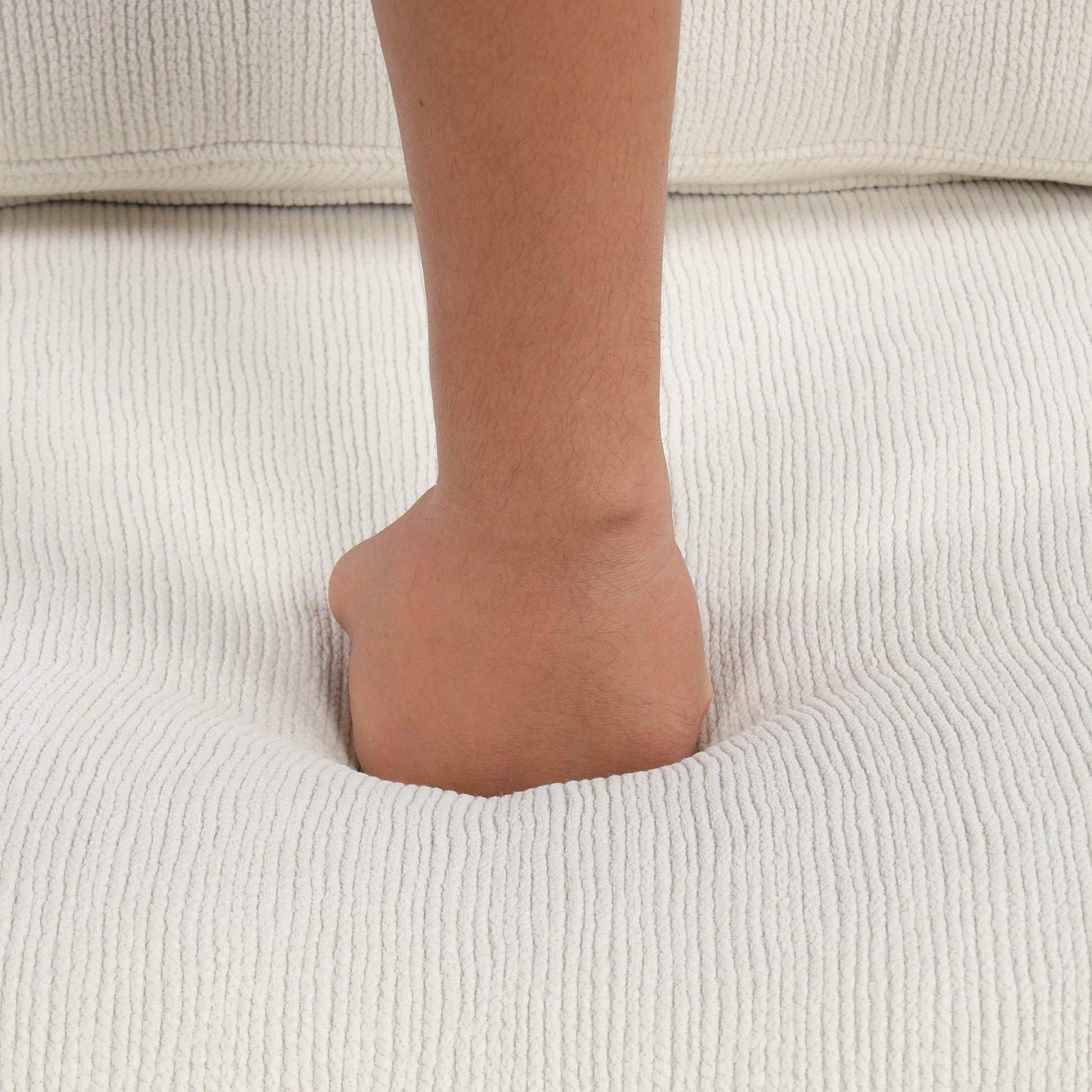 Hand pressing into soft creamcolored corduroy fabric sofa