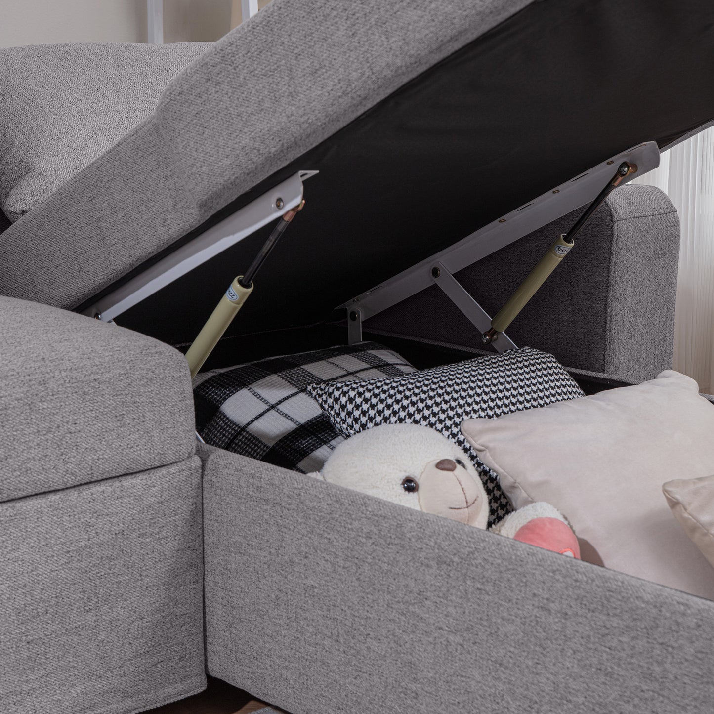 Grey fabric sectional sofa with open storage revealing blankets and a teddy bear