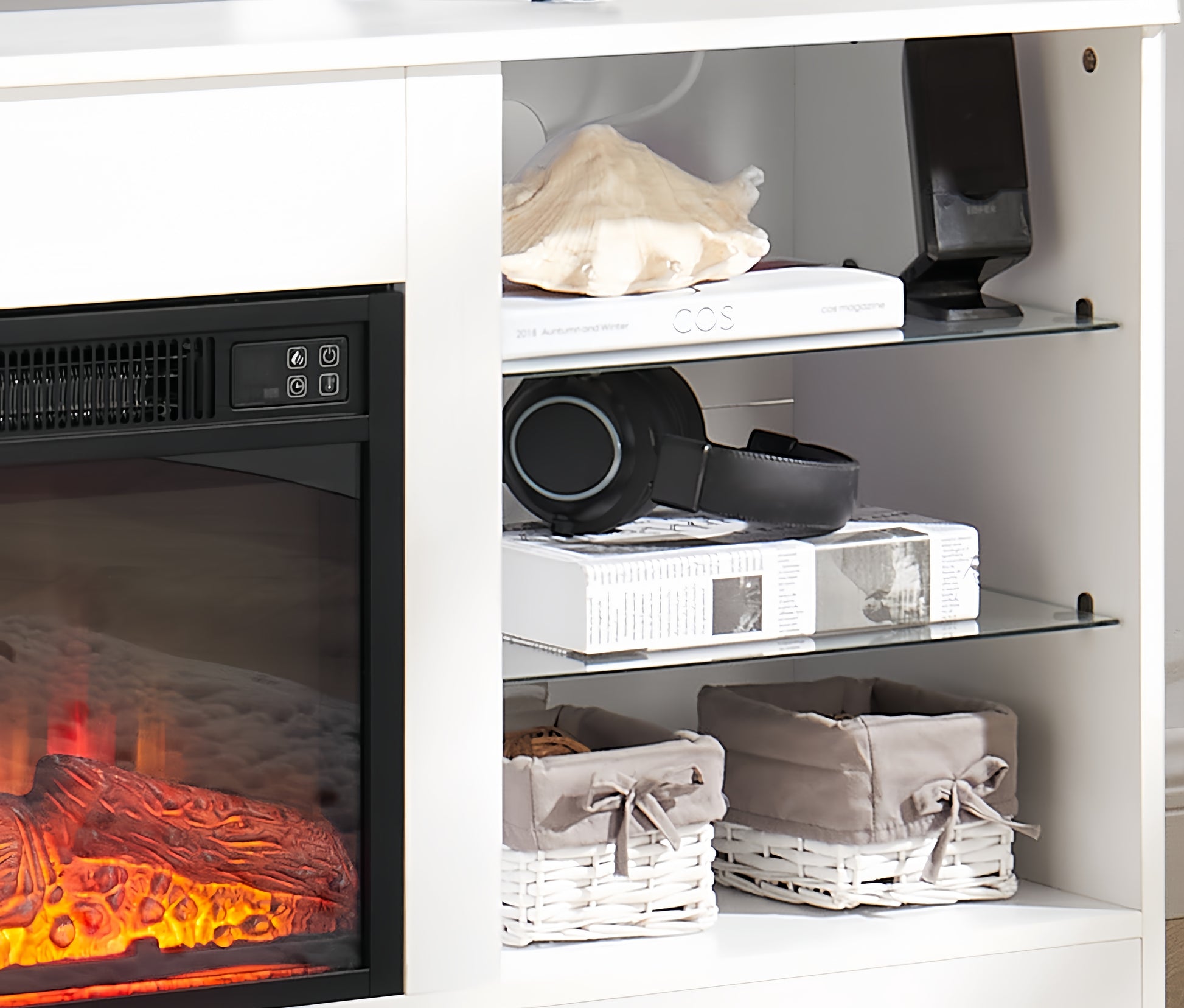 White media console with electric fireplace and glass shelves holding books and headphones