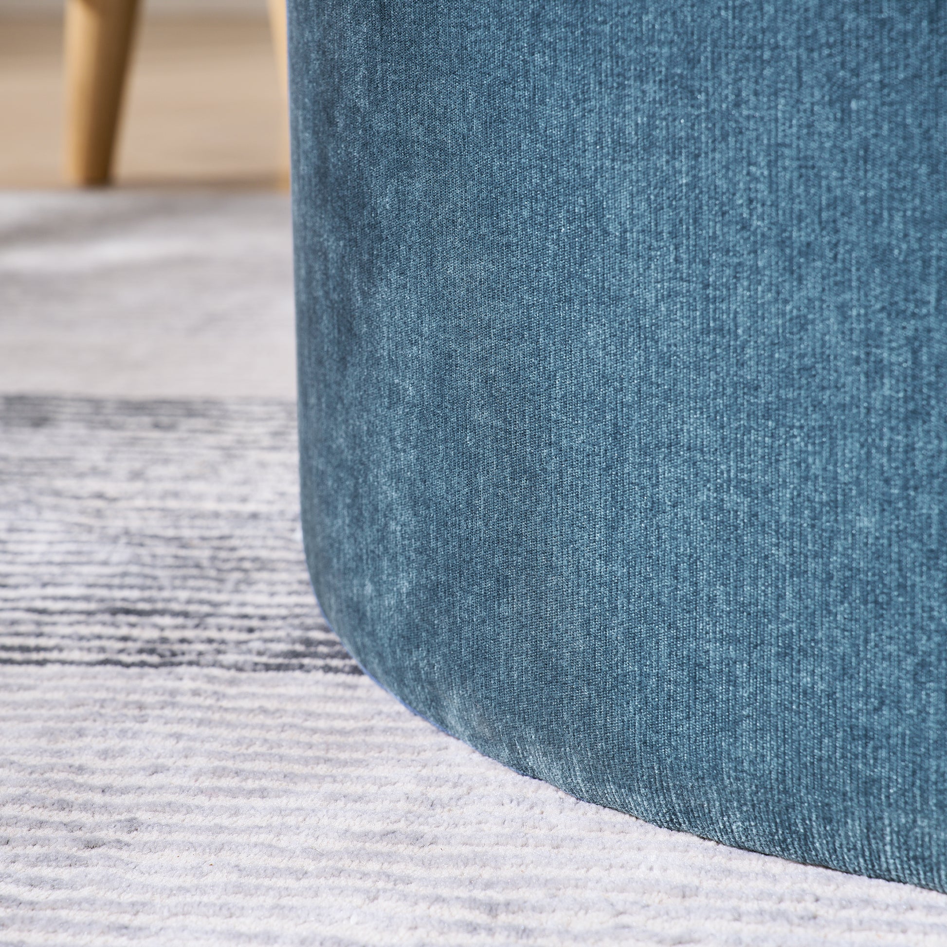 Closeup of textured teal velvet fabric on a modern ottoman with light wood leg in background