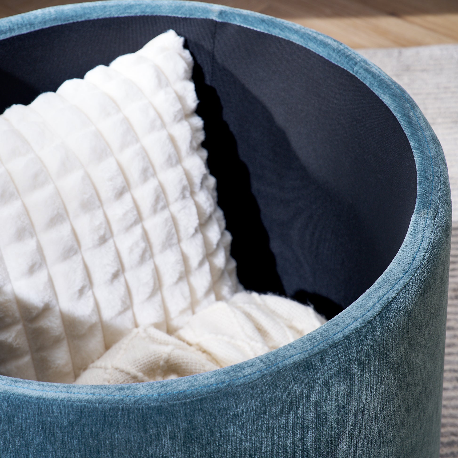 Teal velvet storage ottoman with textured white pillow and cozy throw blanket