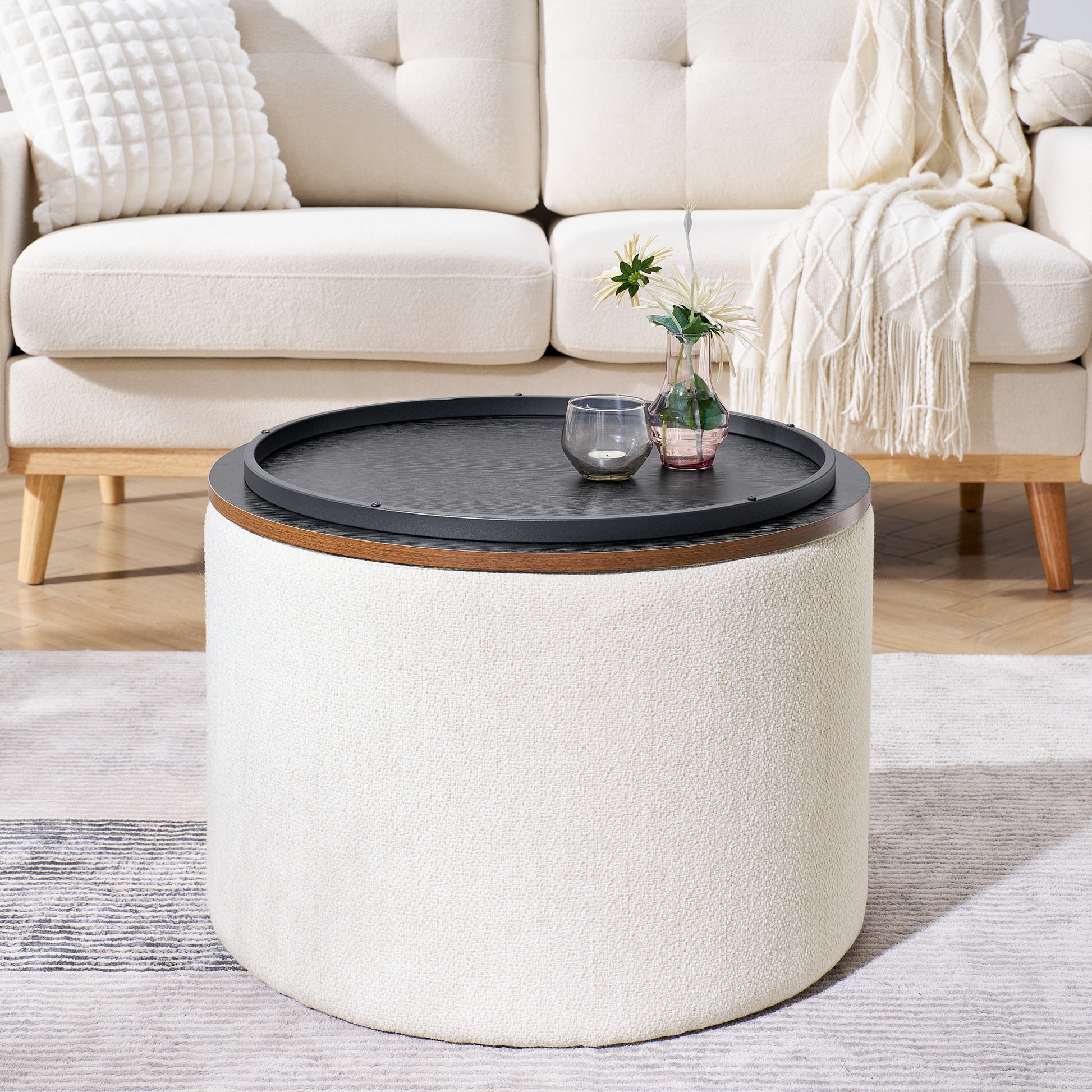 Round cream boucle ottoman coffee table with black wood top and decorative glass items